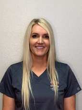 A woman in a blue scrub top is smiling for the camera.
