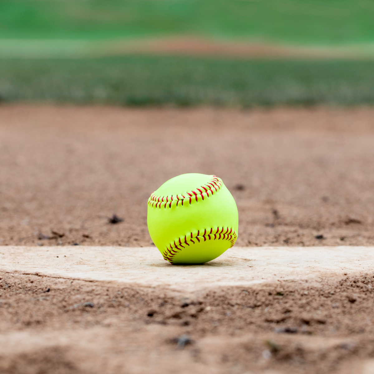 A yellow baseball is sitting on the base of a baseball field.