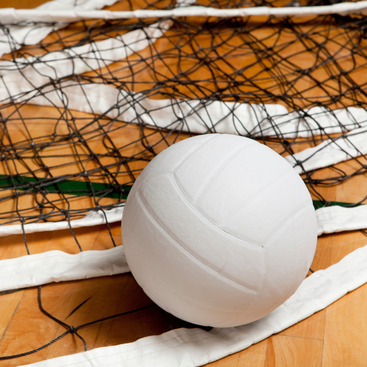 A volleyball is laying on the floor next to a net