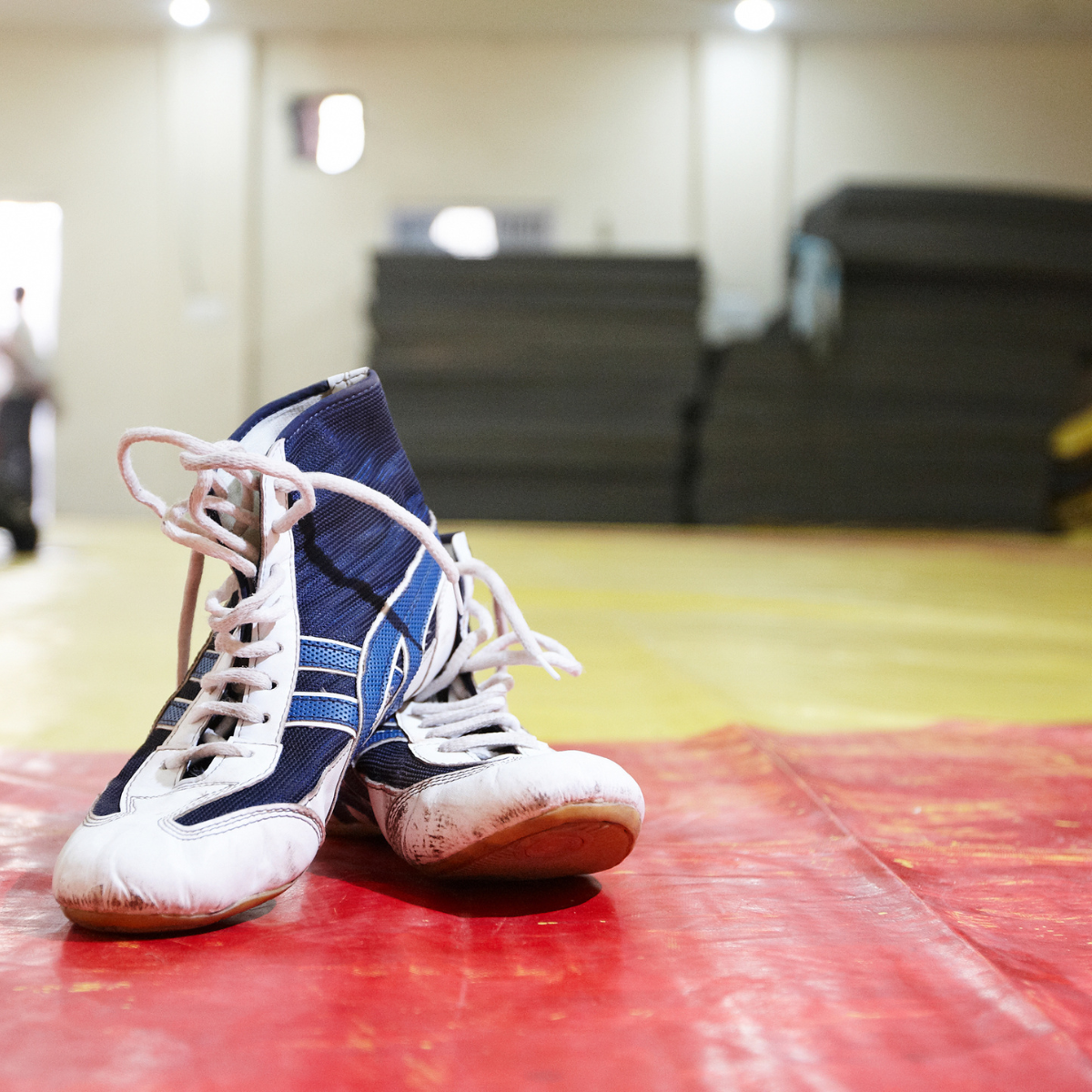 A pair of blue and white wrestling shoes on a red mat