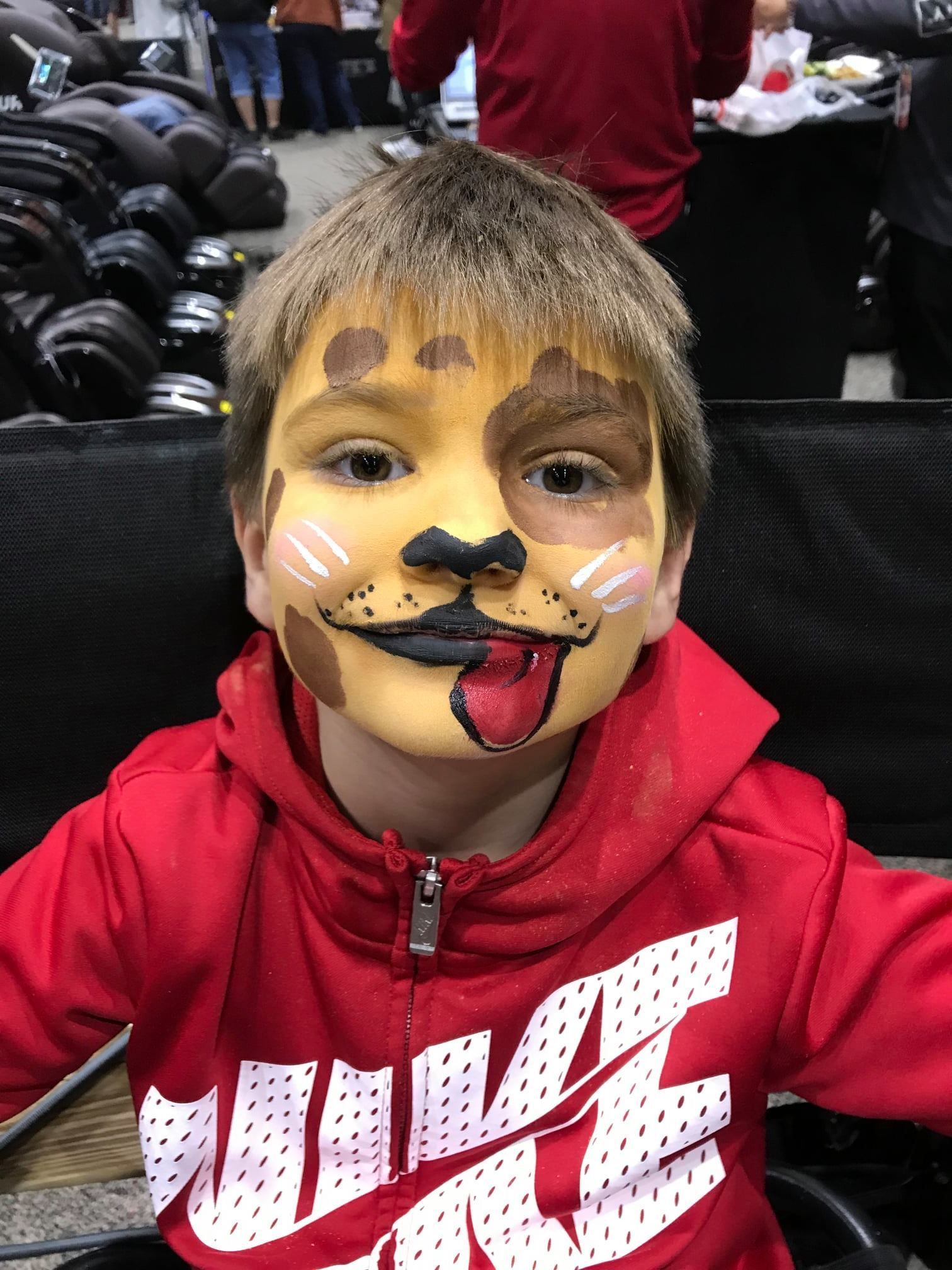 A person wearing a bright red Nike hoodie with a dog-themed face painting, including a tongue design on the chin.