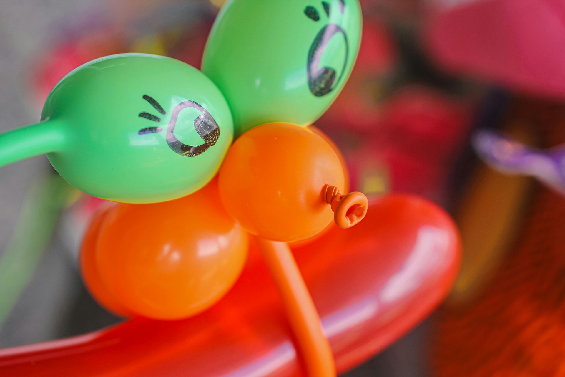 A close-up of a balloon sculpture featuring two green balloons with hand-drawn eyes, orange balloons, and a red base.