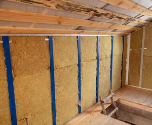 A ladder is sitting on the floor next to a wall with insulation on it.