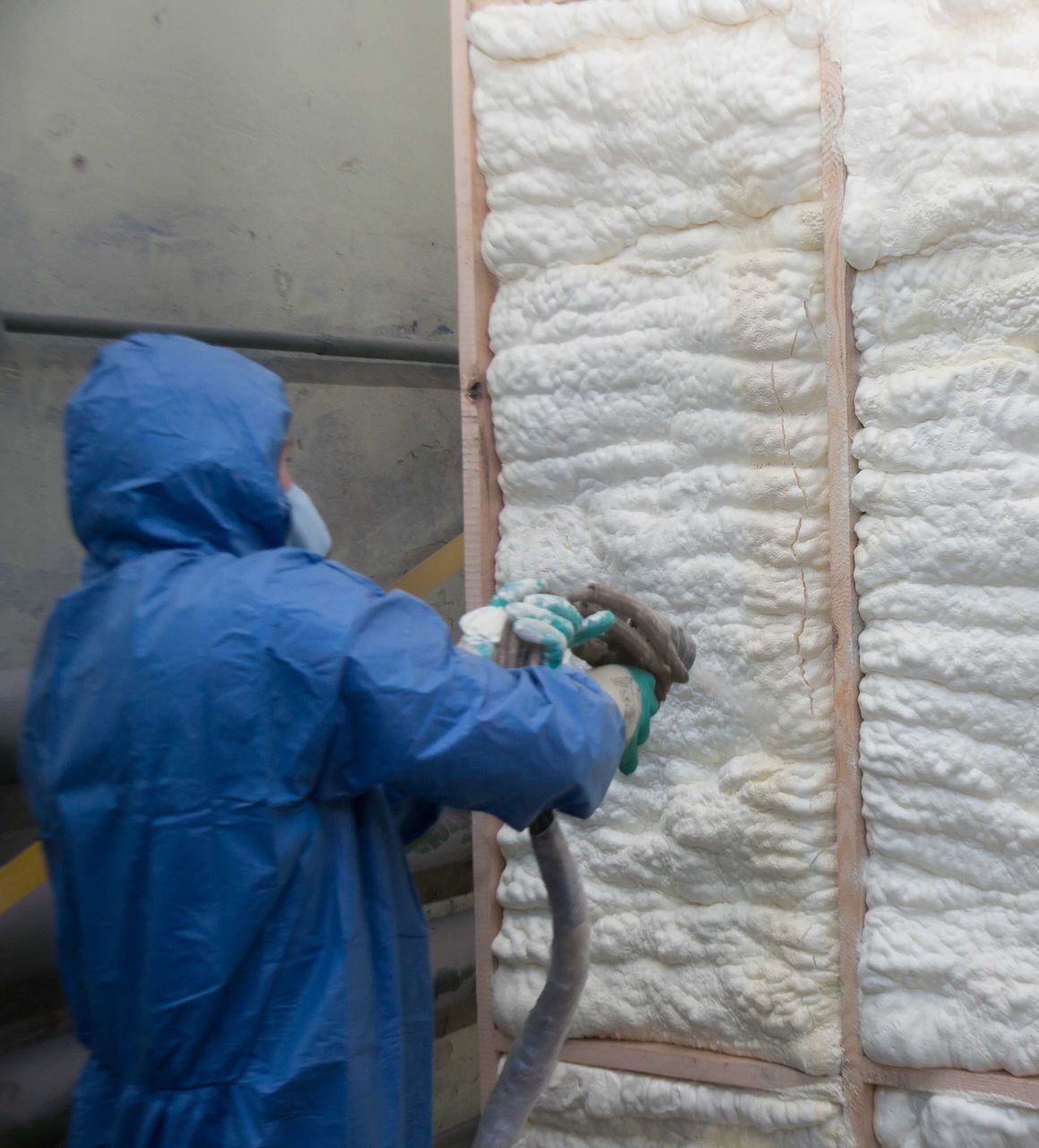 A man in a blue suit is spraying foam on a wall