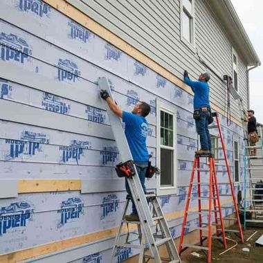 A man is installing siding on the side of a building.