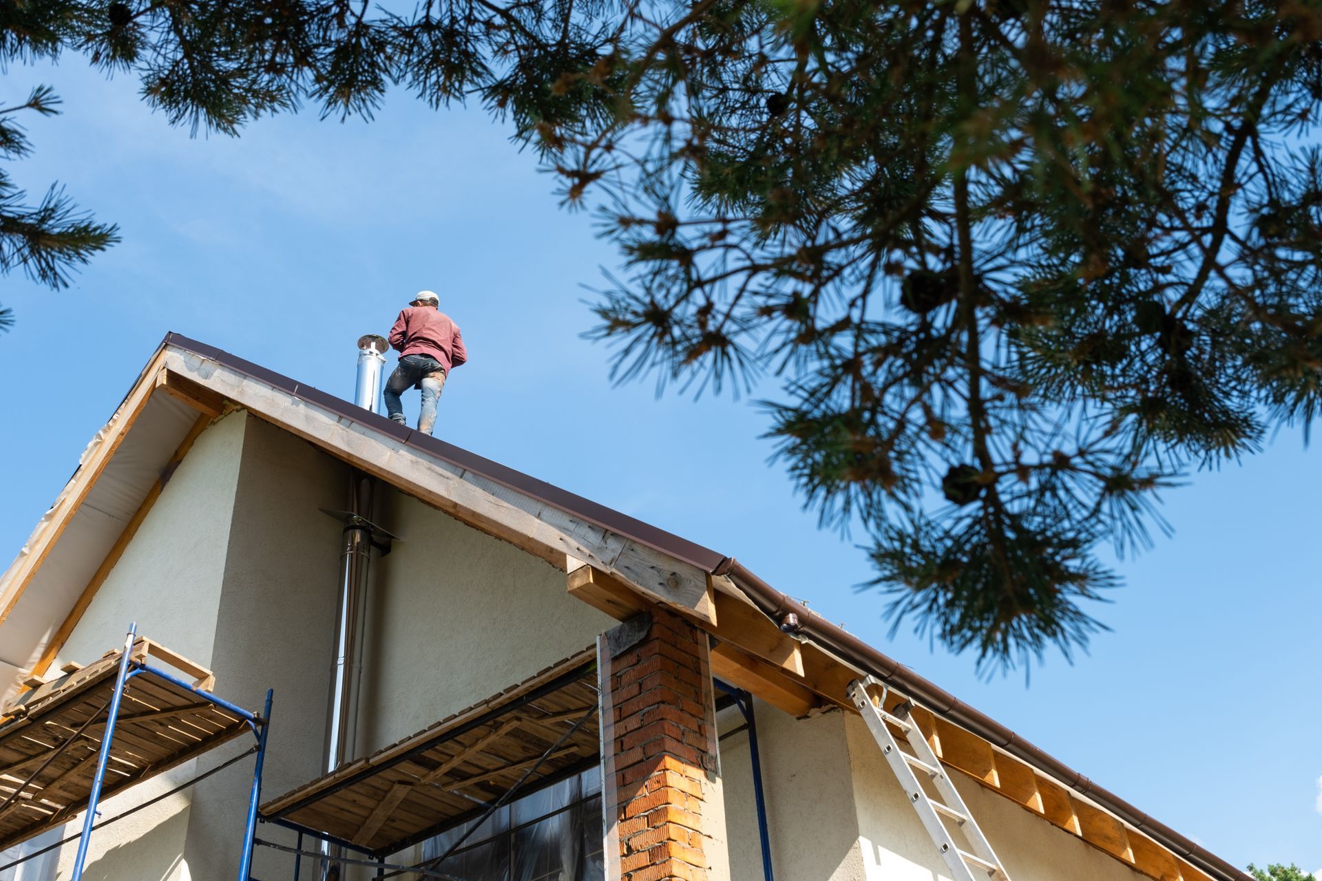 Worker stands on a house roof next to a metal chimney pipe - D&B Roofing