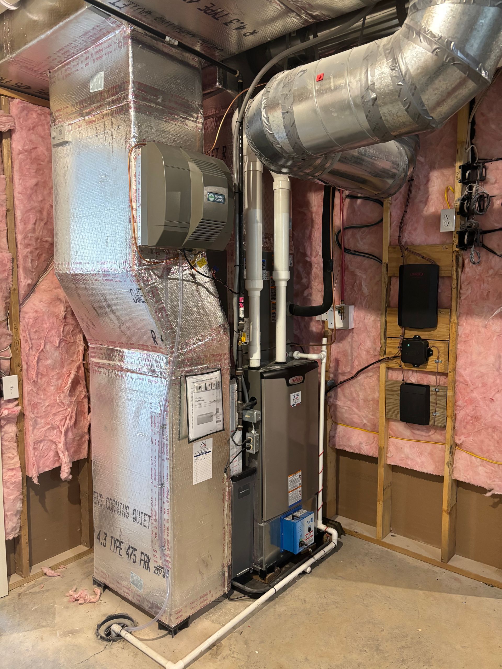 HVAC system in a basement. Silver furnace and ductwork, pink insulation, and wooden studs are visible.