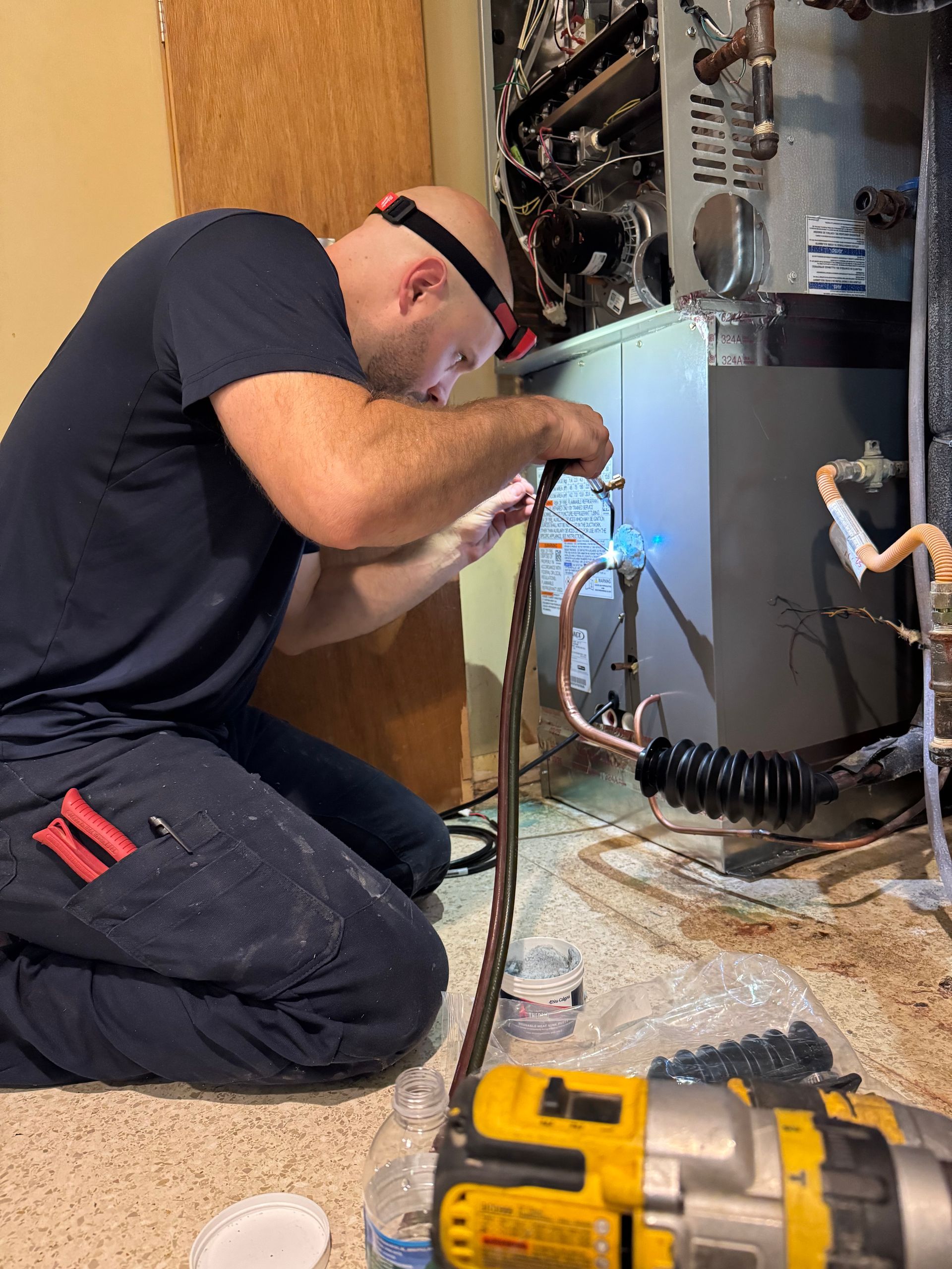 A person working on an HVAC unit, using a torch. They wear a headlamp.