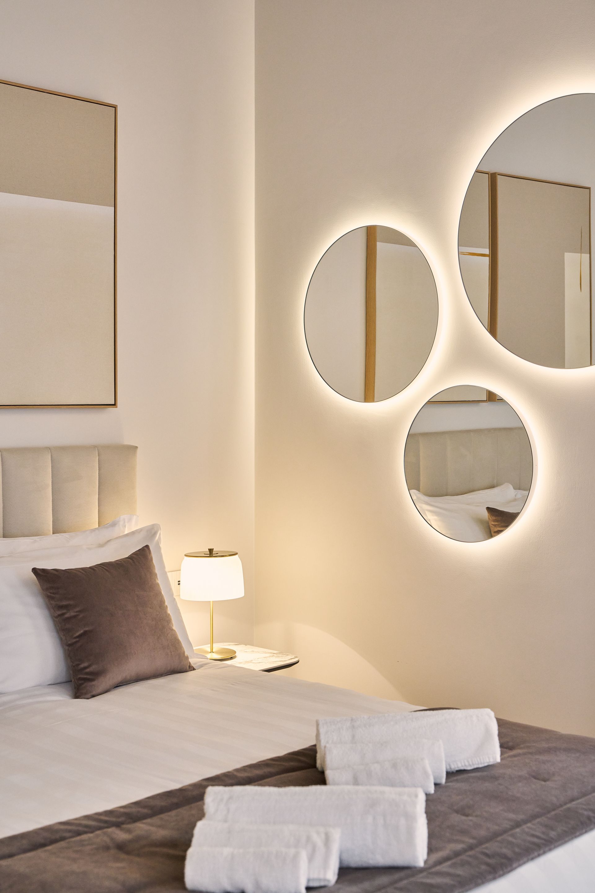 Modern bedroom with bed, beige walls, circular mirror decor, and warm bedside lighting