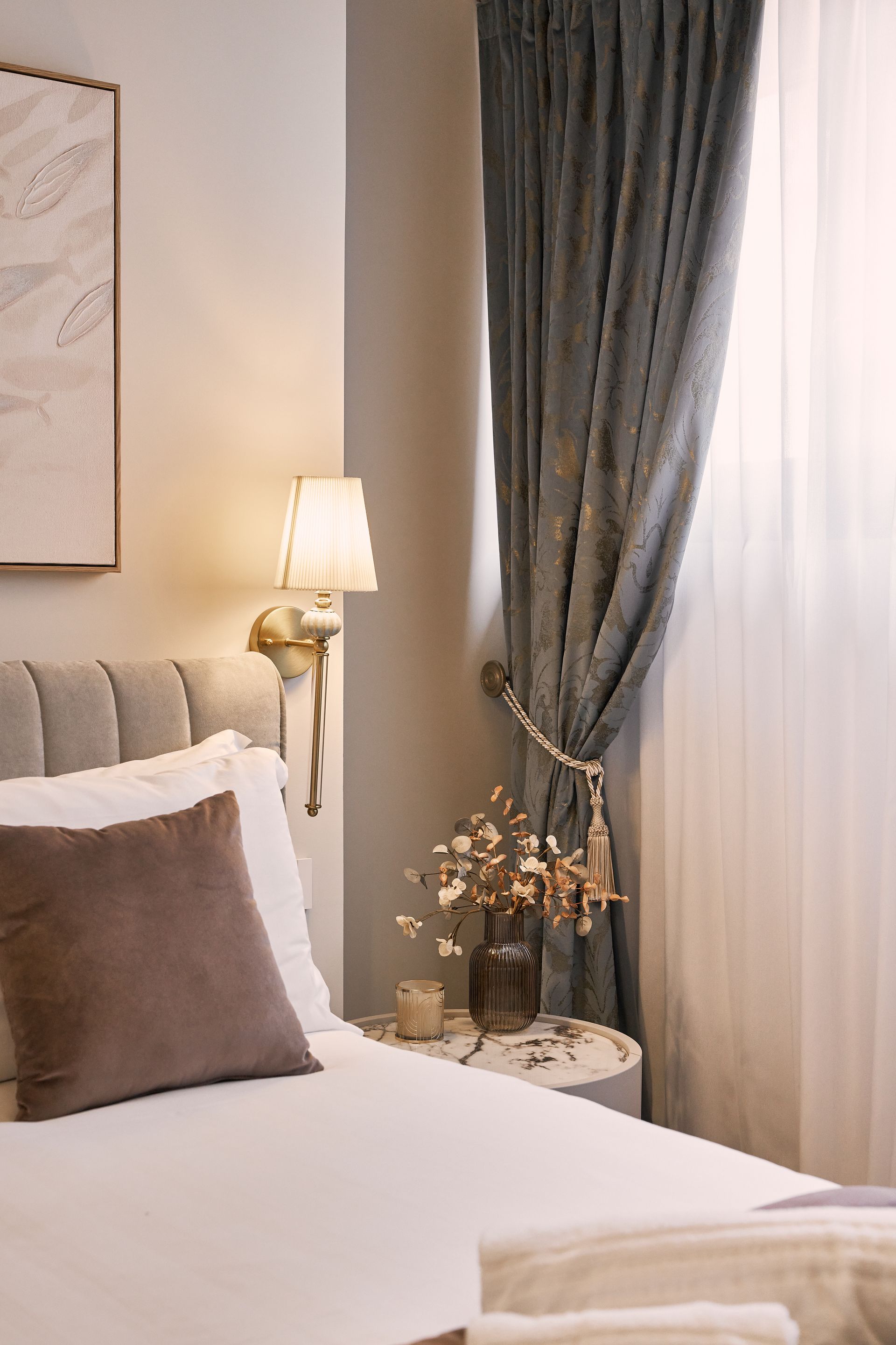 Cozy bedroom corner with a bed, bedside lamp, dark curtain, and soft neutral decor.