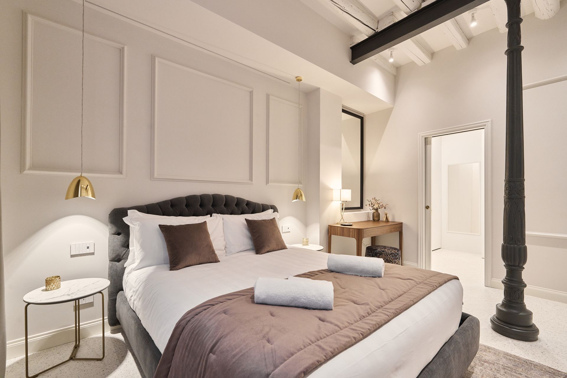 Stylish bedroom with a bed, bedside lamps, a vanity table, and a large black column.