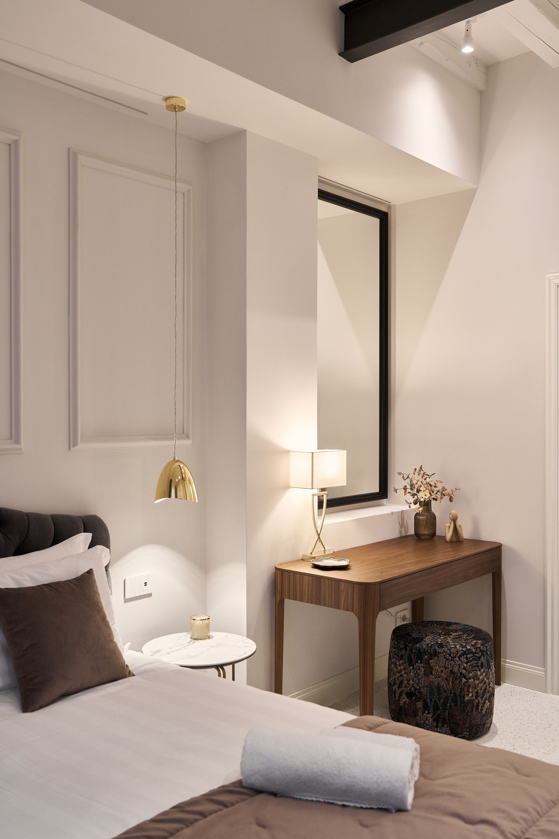Cozy bedroom with white bedding, wooden desk, mirror, lamp, and gold pendant light