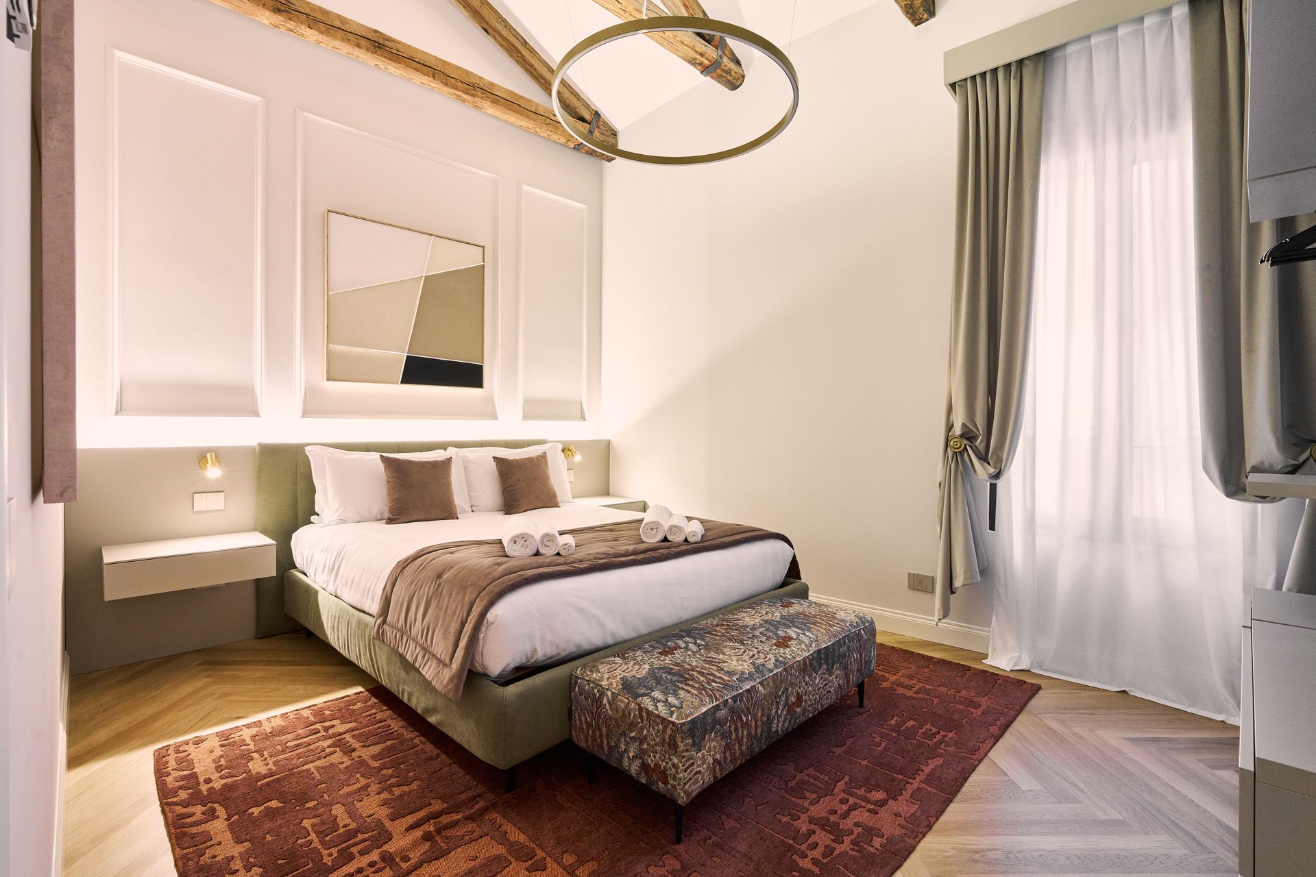 Elegant bedroom with a bed, bench, wall mirror, and tall curtained window.