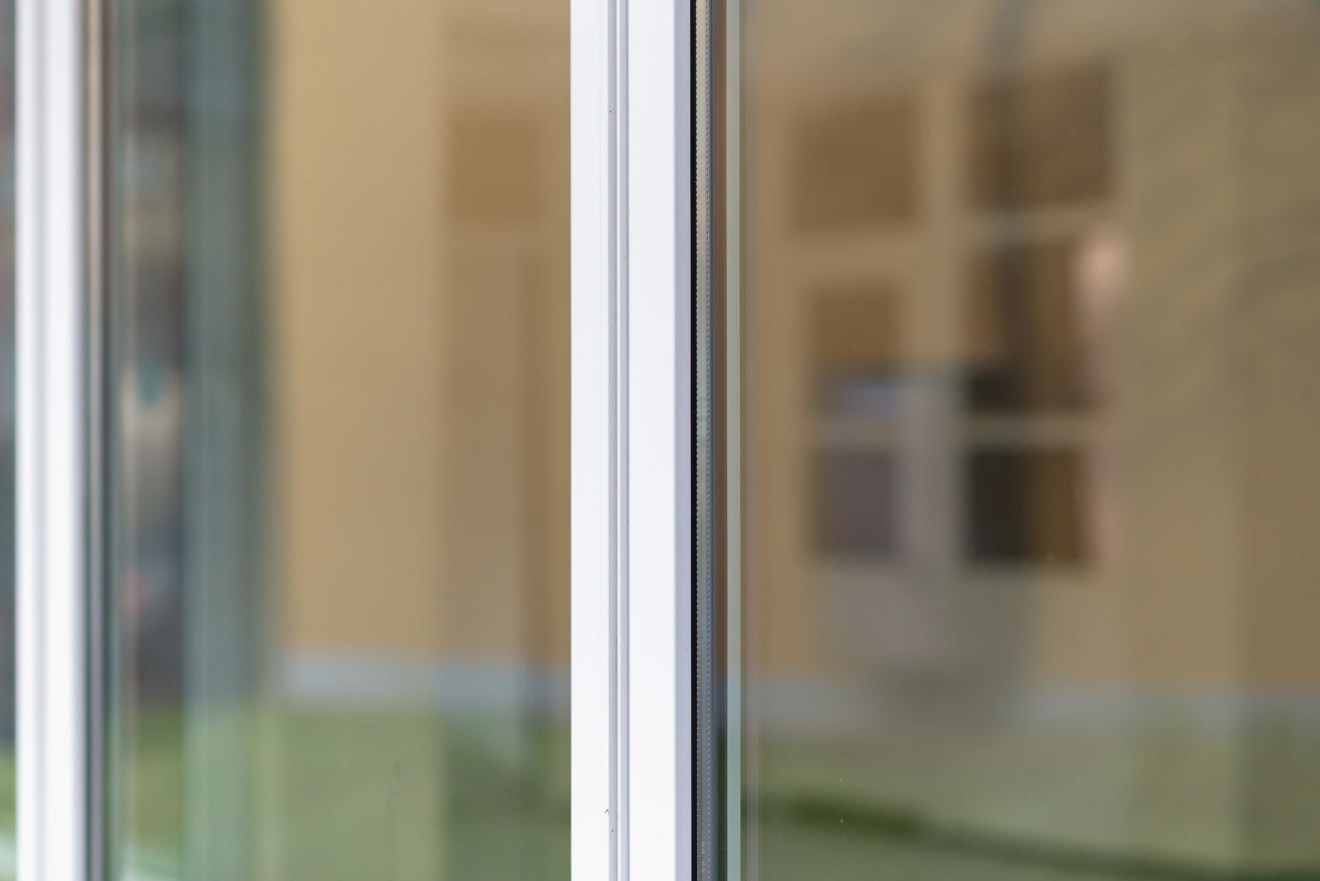 Gros plan sur un cadre de fenêtre blanc avec un panneau de verre, reflétant un intérieur flou aux couleurs claires.
