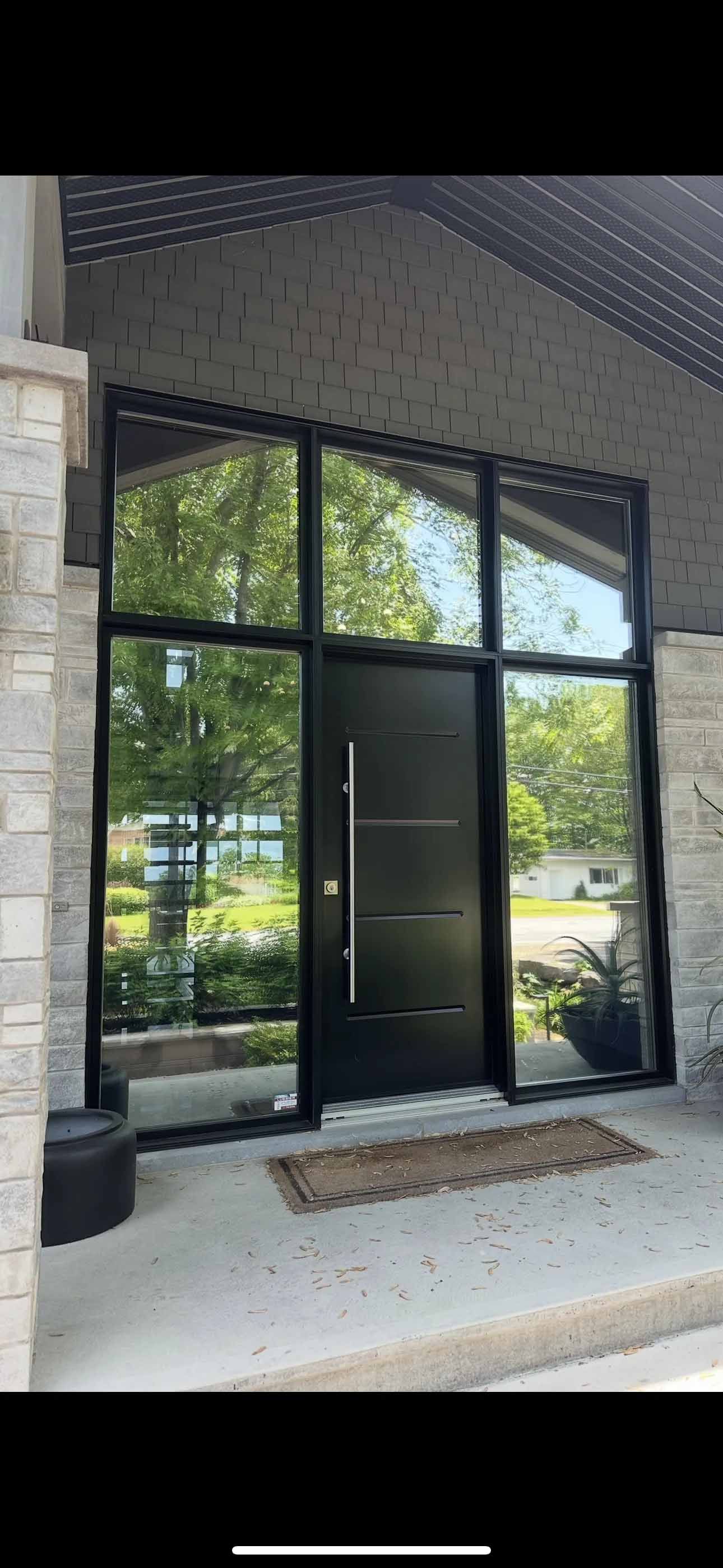 Porte d'entrée moderne noire avec imposte latérale, sous une façade en briques neutres.