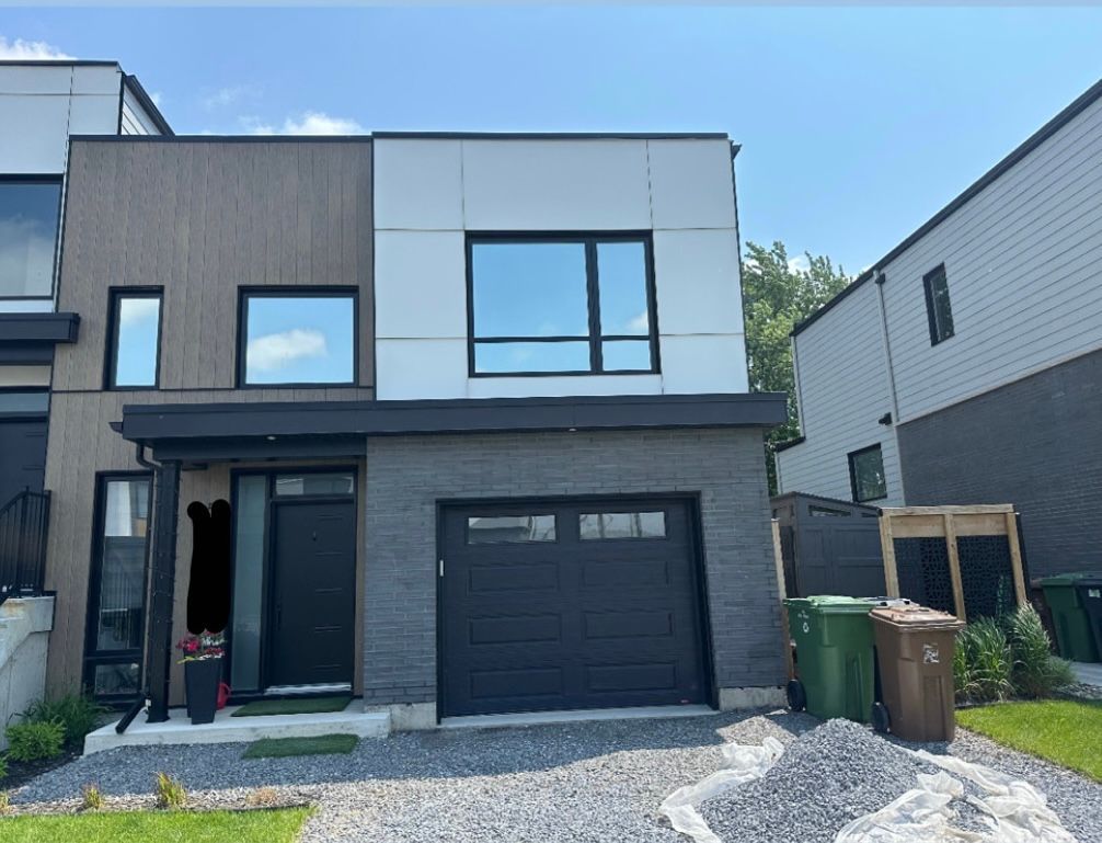 Maison de ville moderne avec briques grises, porte de garage noire et bardage blanc et gris.
