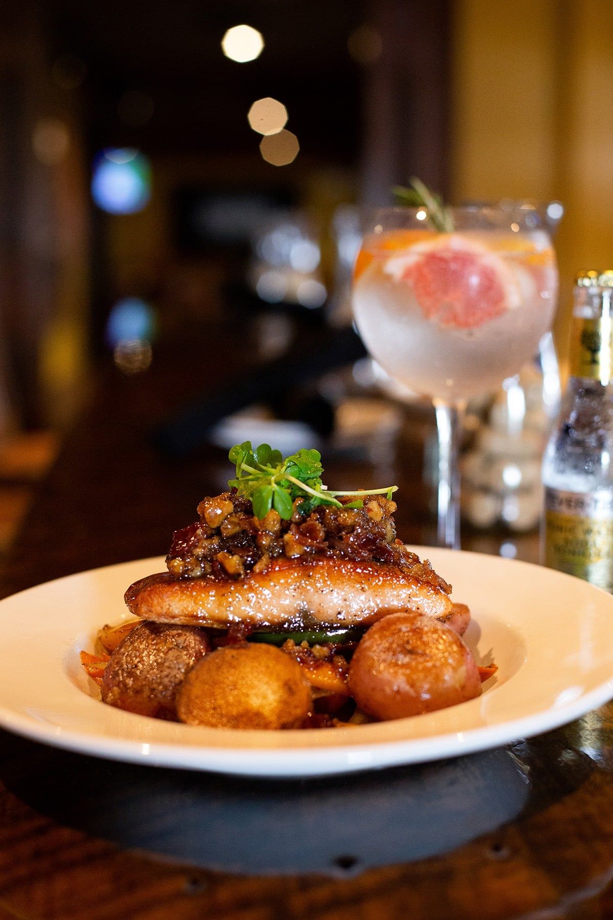 Plate of food with potatoes and a drink on a bar.