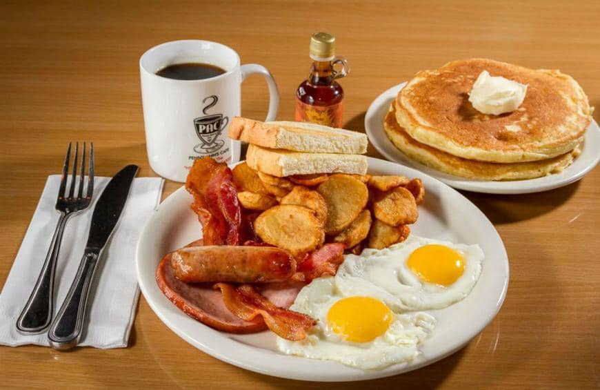 Breakfast plate with eggs, bacon, sausage, potatoes, toast, pancakes, coffee, and maple syrup.
