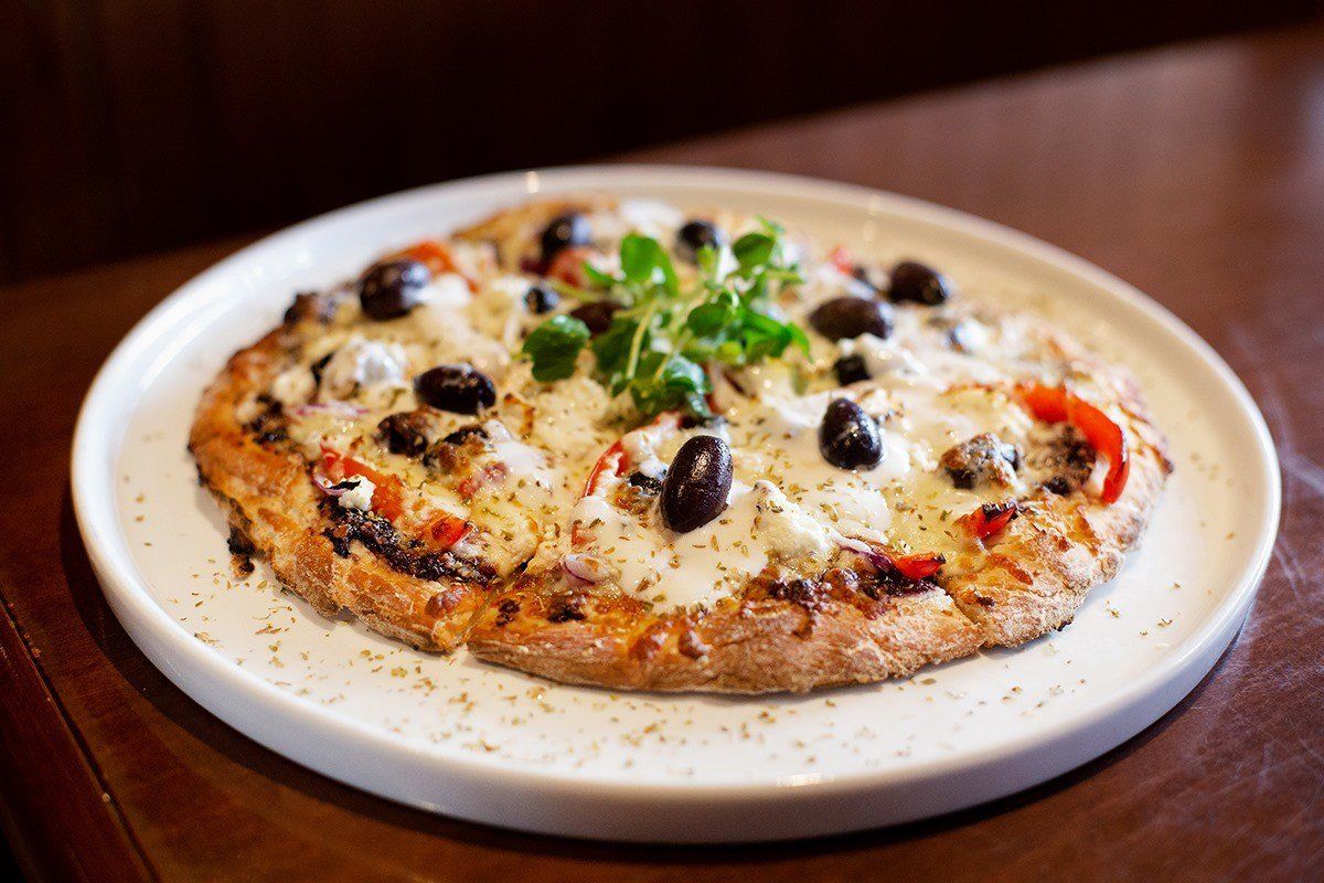 Pizza topped with olives, cheese, red peppers, and herbs on a white plate.