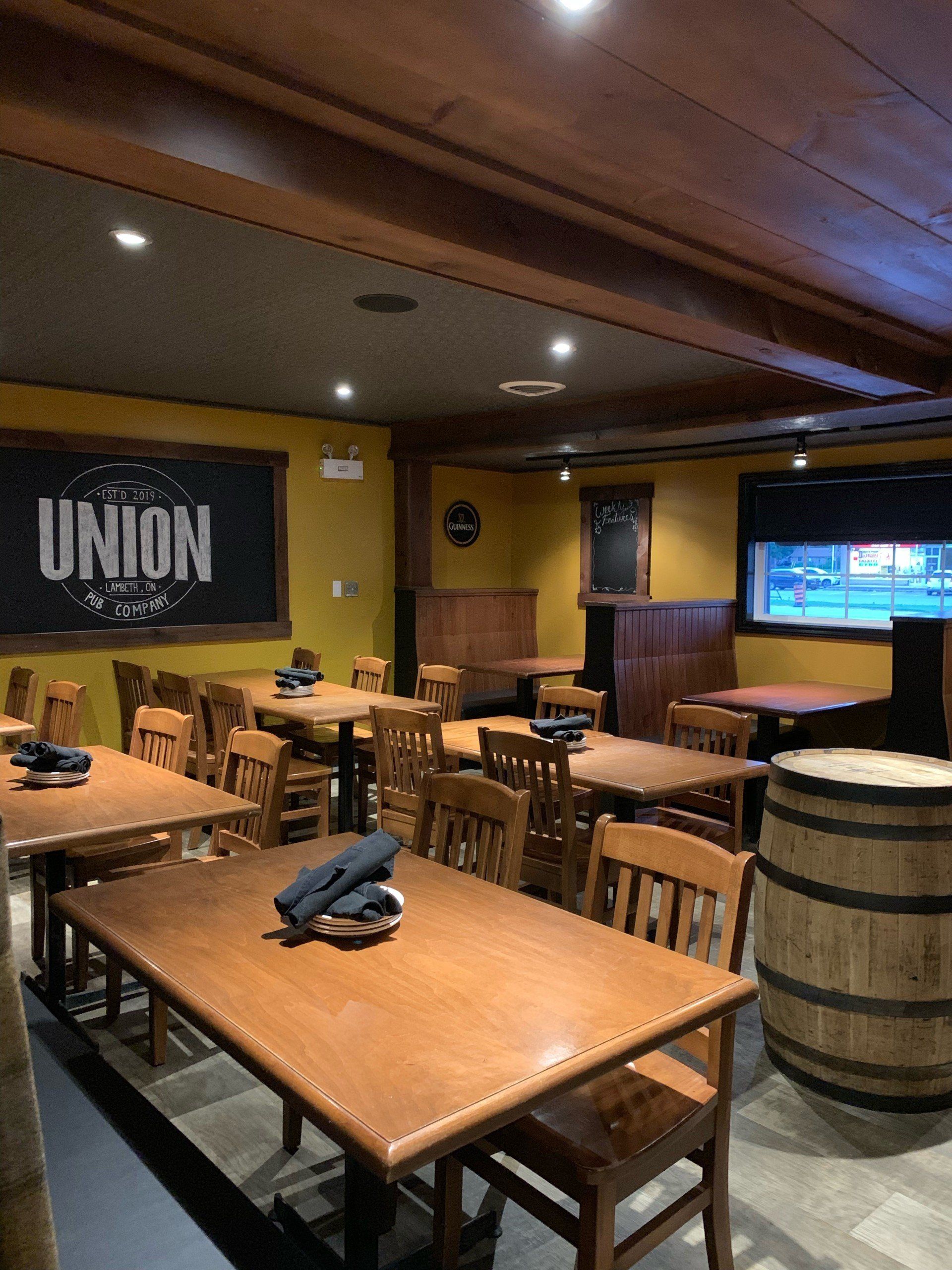Interior of a rustic pub with wooden tables and chairs, barrels, and a chalkboard that says