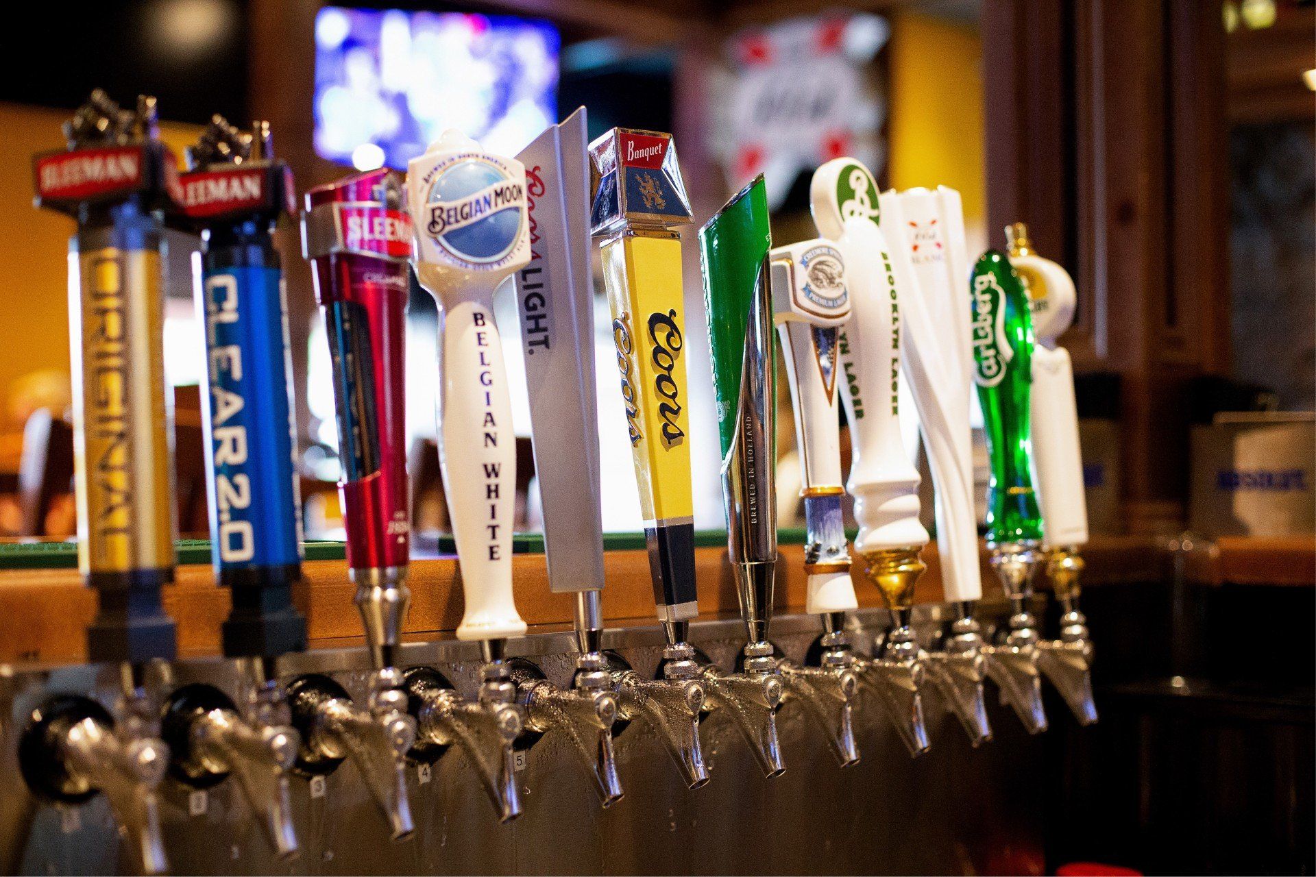 Beer taps at a bar, various brands displayed on handles, dimly lit interior.