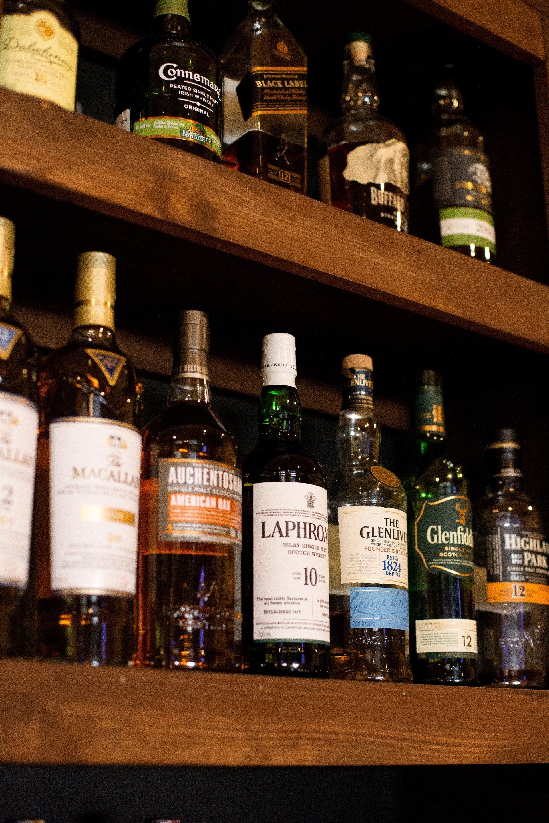 Whiskey bottles on wooden shelves in a bar, including Macallan, Laphroaig, and Glenfiddich brands.