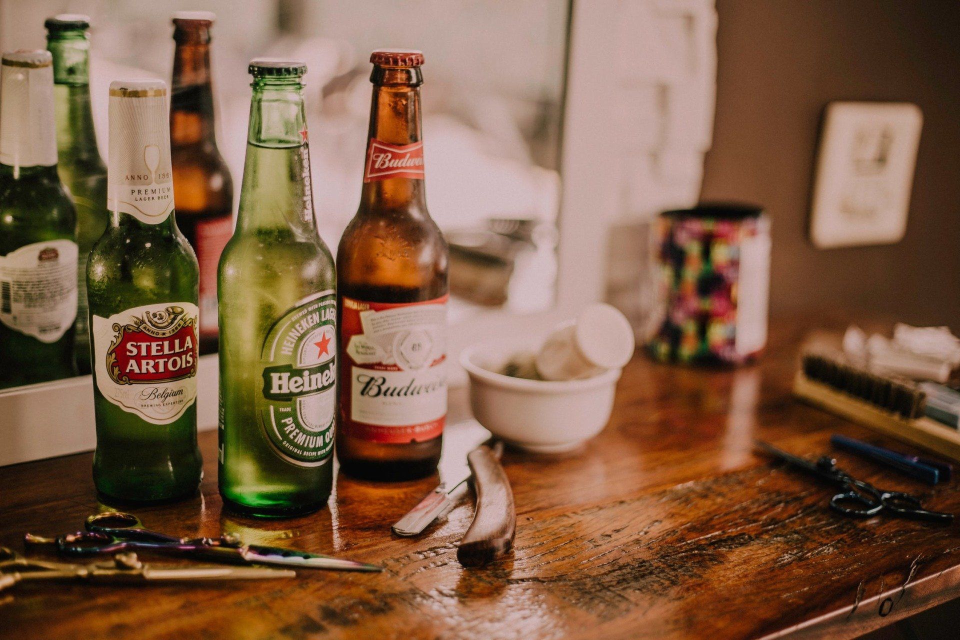 Beer bottles on a wooden table with scissors and a small bowl; a barber shop interior.