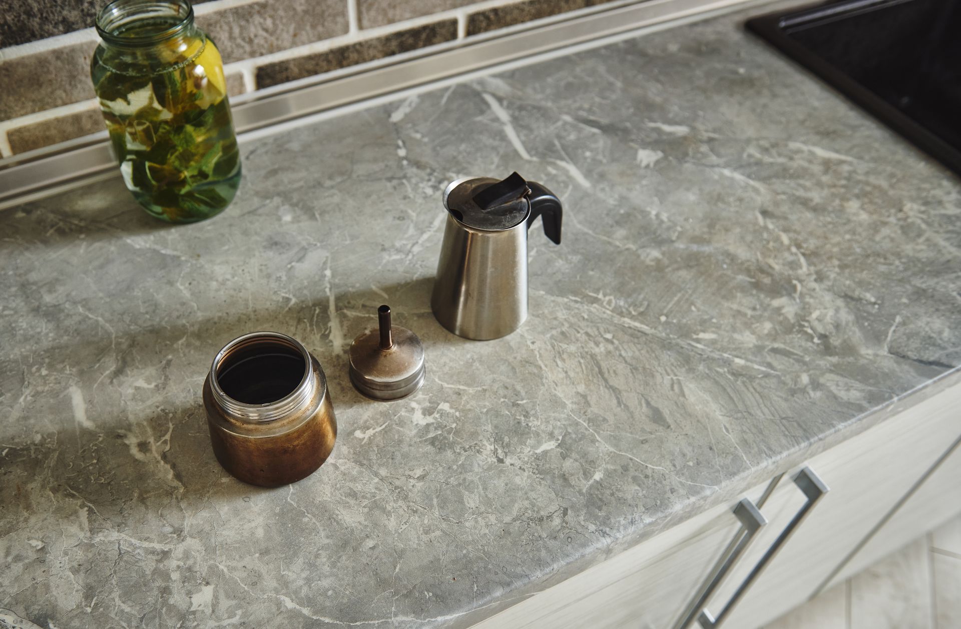 Coffee maker parts on a gray marbled countertop in a kitchen.