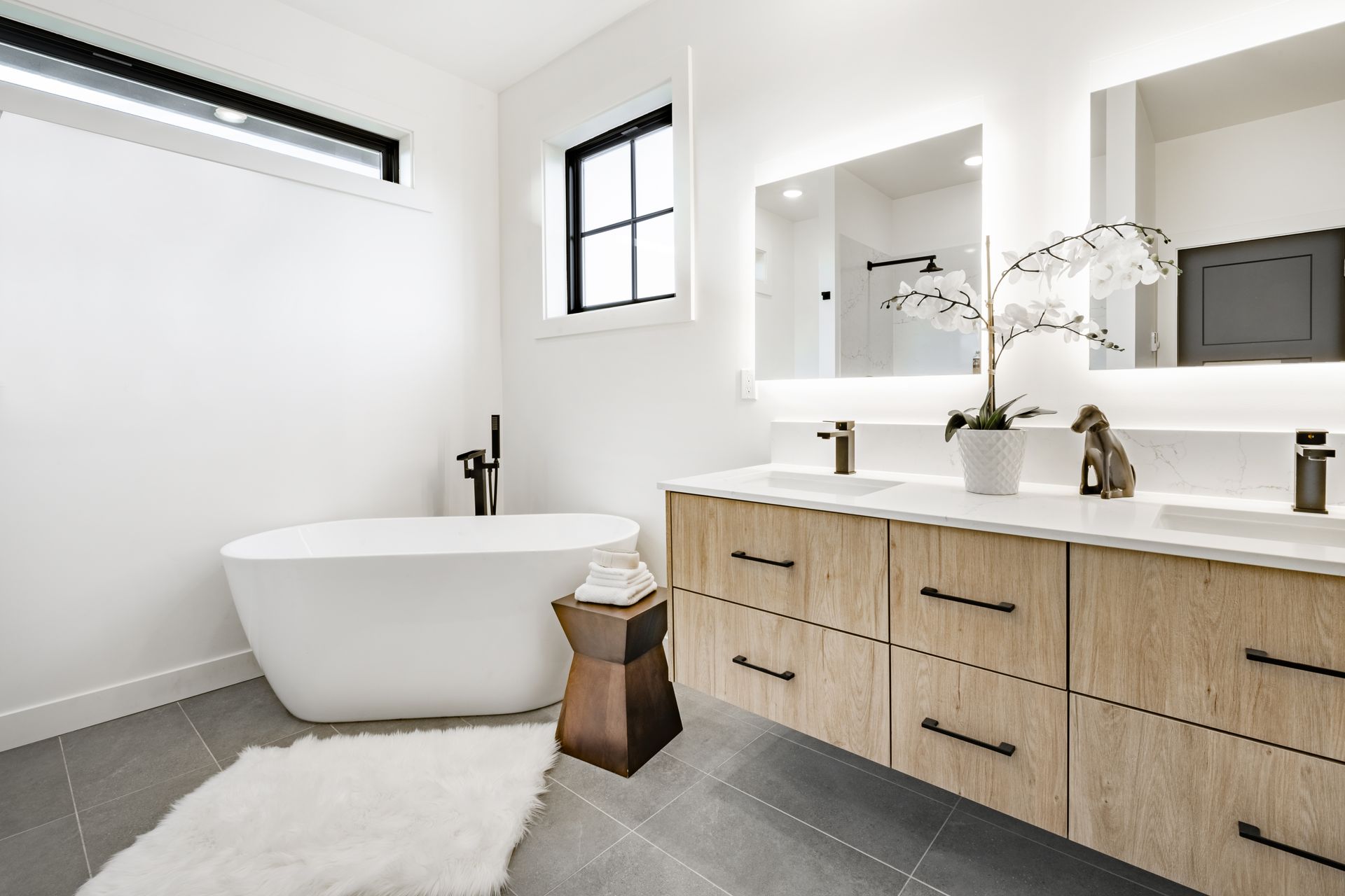 Modern bathroom with a white tub, wooden vanity, and large mirrors.