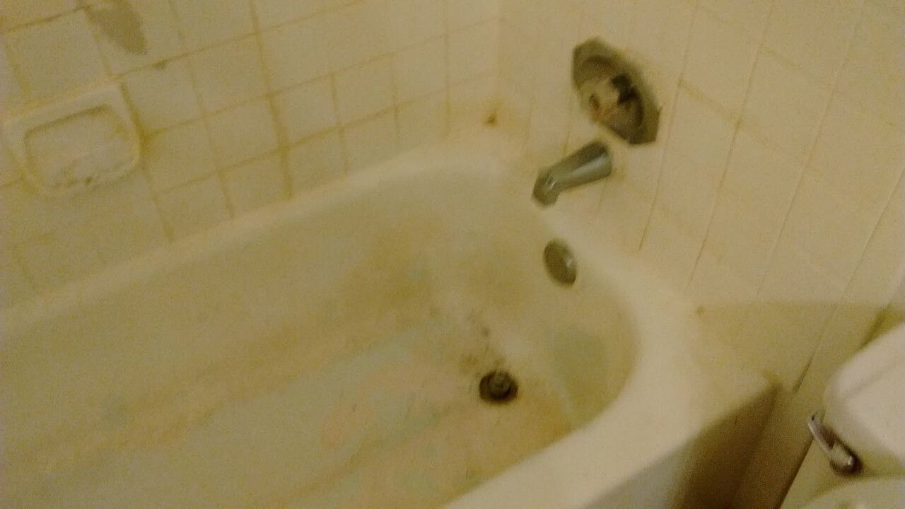 Dirty, off-white bathtub with stained tiles and fixtures; soap dish on the wall.