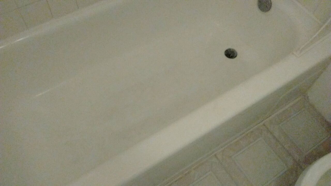 Off-white bathtub with drain and faucet, set in a bathroom with beige tiles.