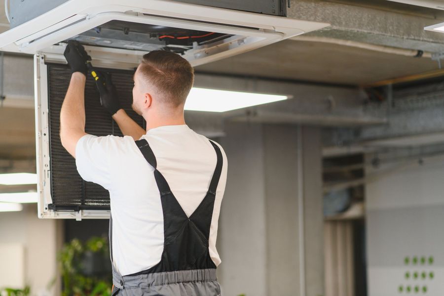 Technician inspecting an open ceiling HVAC vent in a bright indoor space