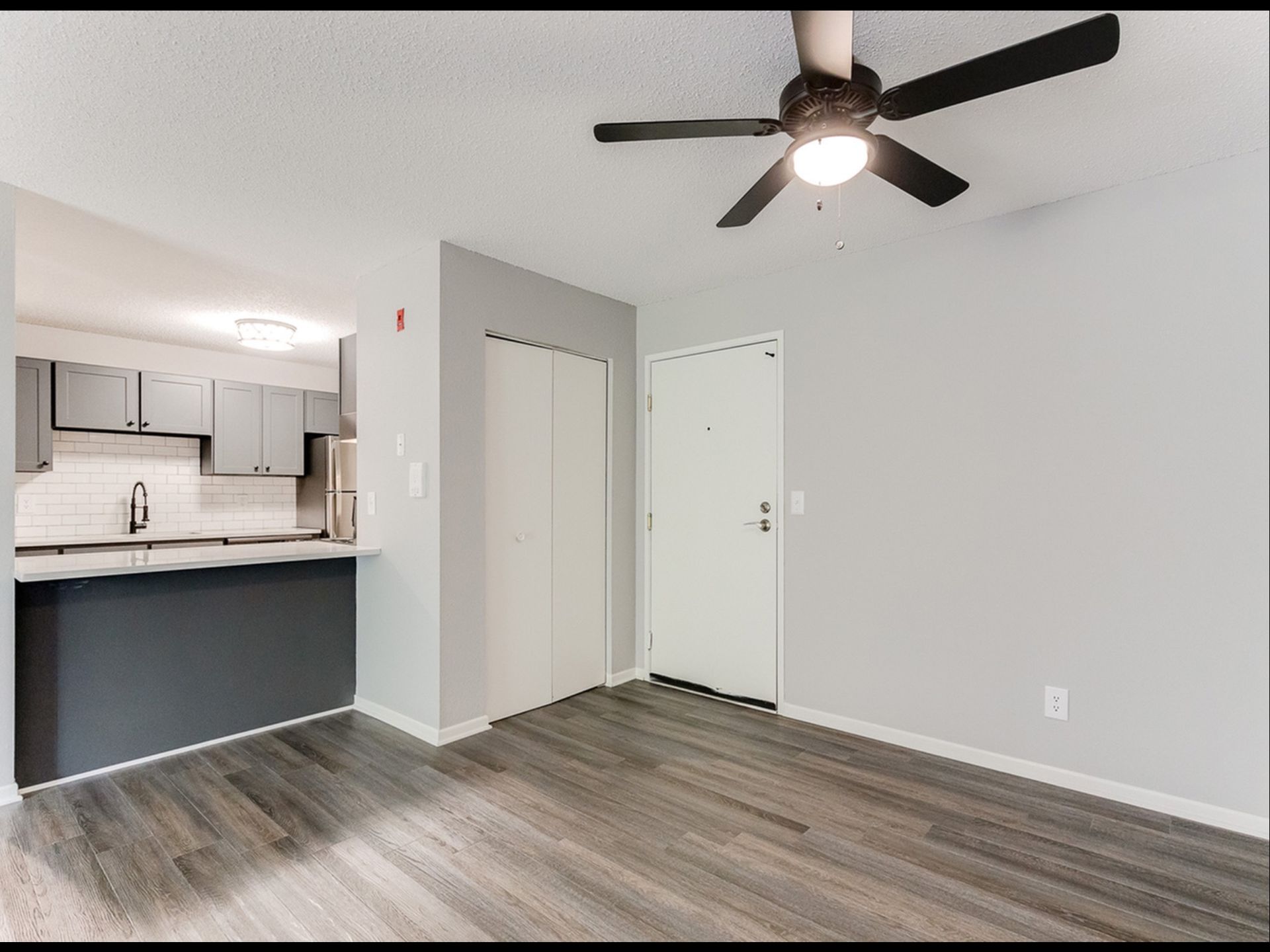 Open-concept apartment interior with kitchen island, gray walls, and a ceiling fan.