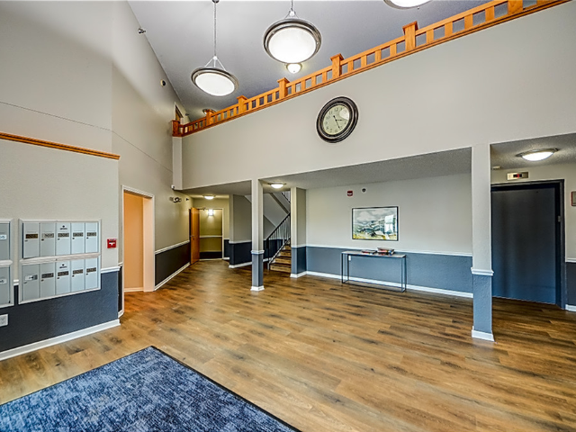 Interior of a residential community lobby with mailboxes, a staircase, and a wall clock.