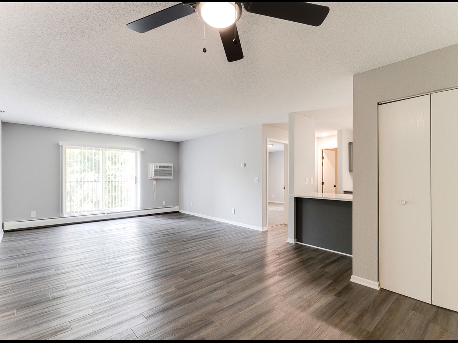 Living room with large window, blinds, window air conditioner, and open kitchen bar.