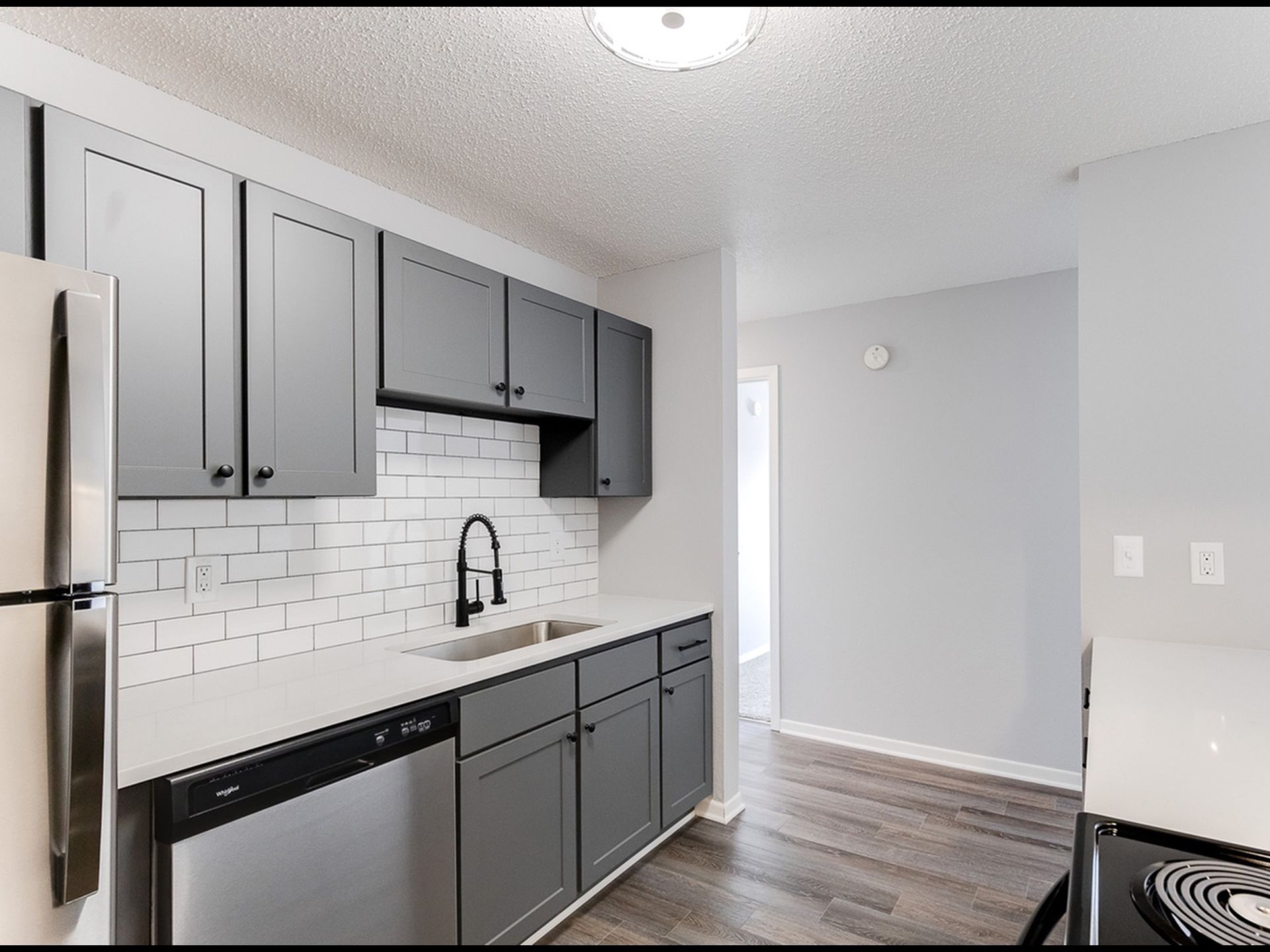Modern apartment kitchen with gray cabinets, white subway tile backsplash, and stainless steel appliances.