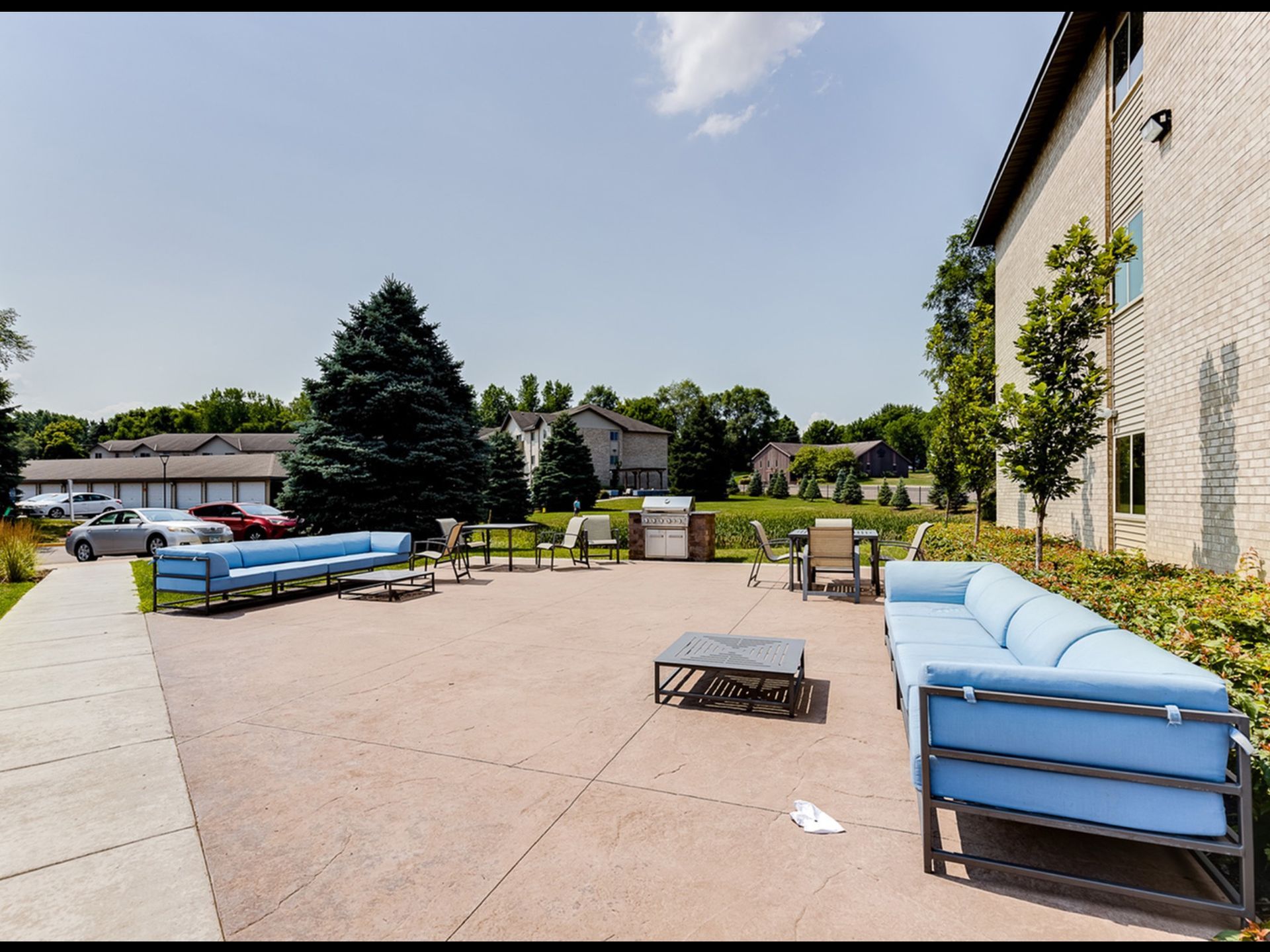 Outdoor communal patio with blue-cushioned seating, tables, and a grill beside an apartment building.