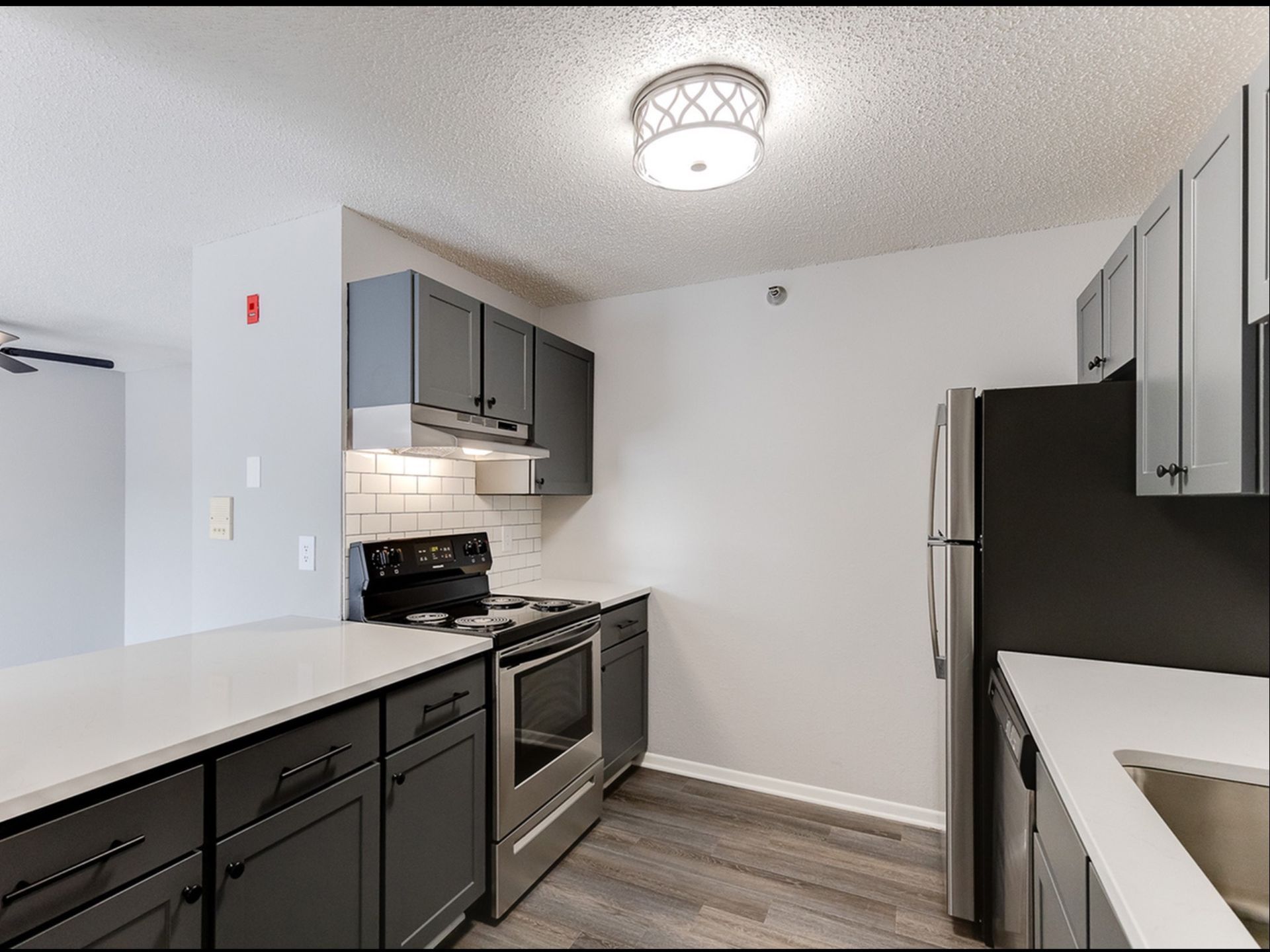 Modern apartment kitchen with gray cabinets, white countertops, and stainless-steel appliances.