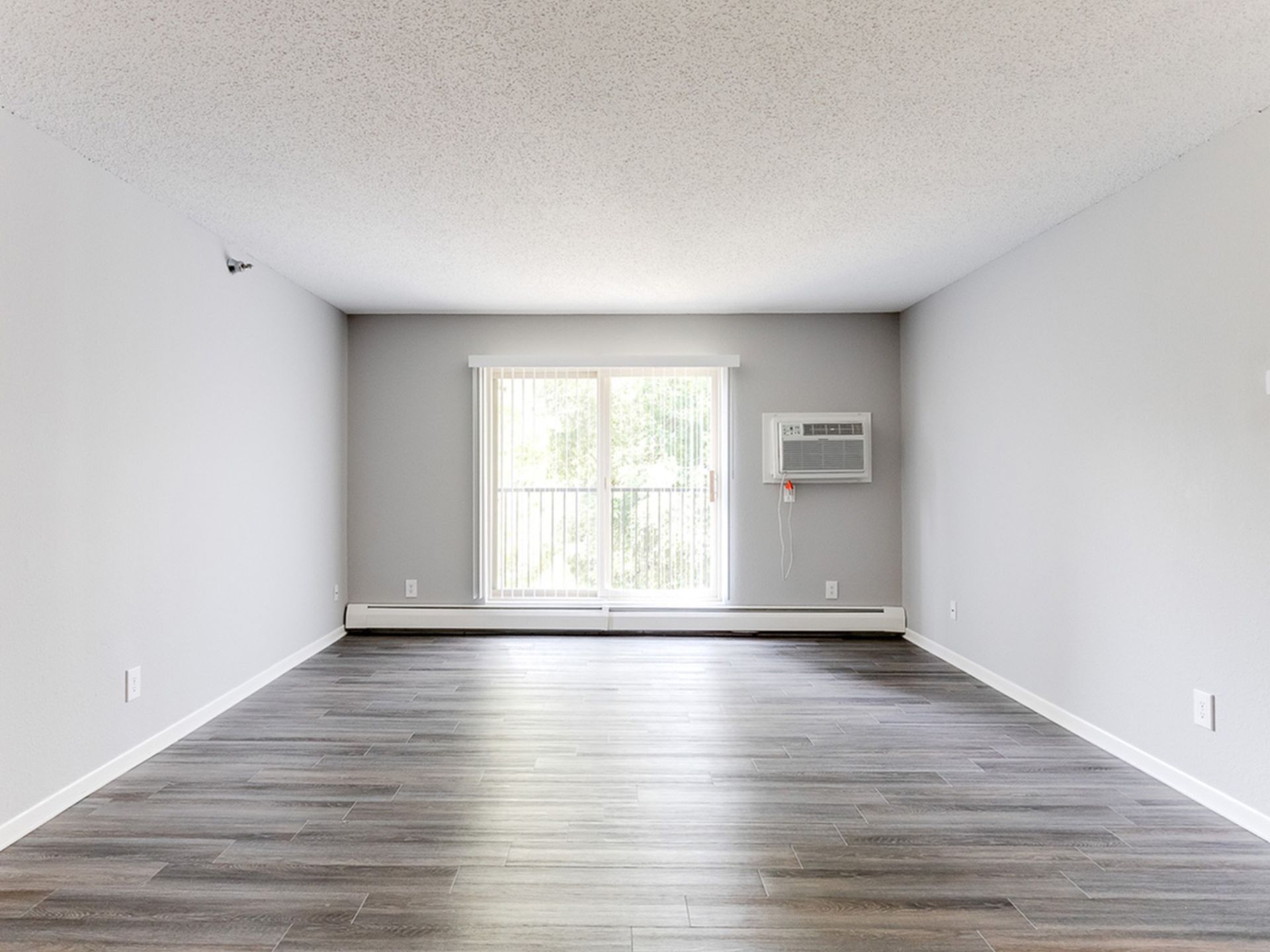 Empty living room in a modern apartment with gray walls, wood-look flooring, and a window AC unit.