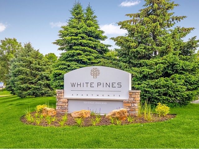 Exterior sign for White Pines Apartments with a landscaped lawn and trees.