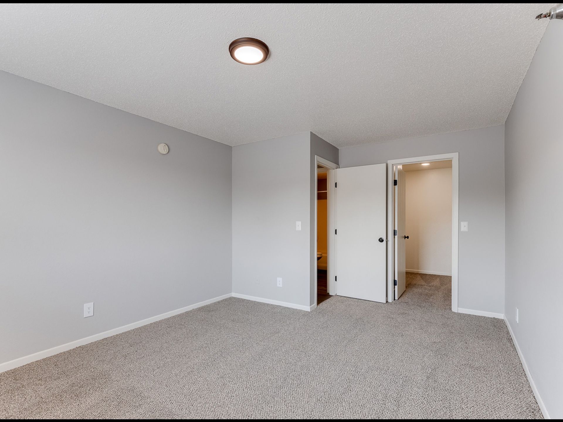 Unfurnished bedroom with light gray walls, beige carpet, and an open doorway to a hallway.