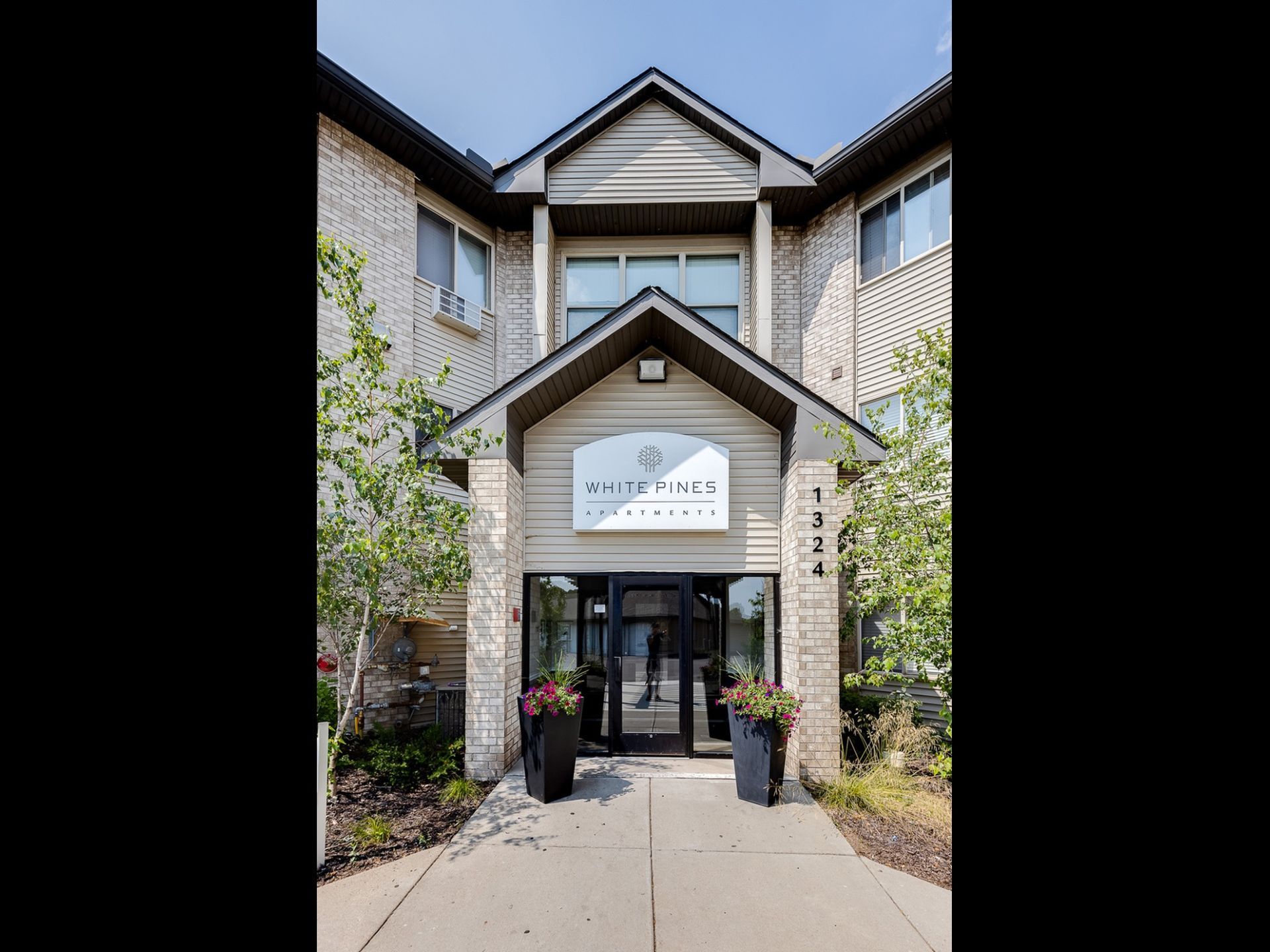 Exterior entrance to White Pines Apartments with a sign and planters.