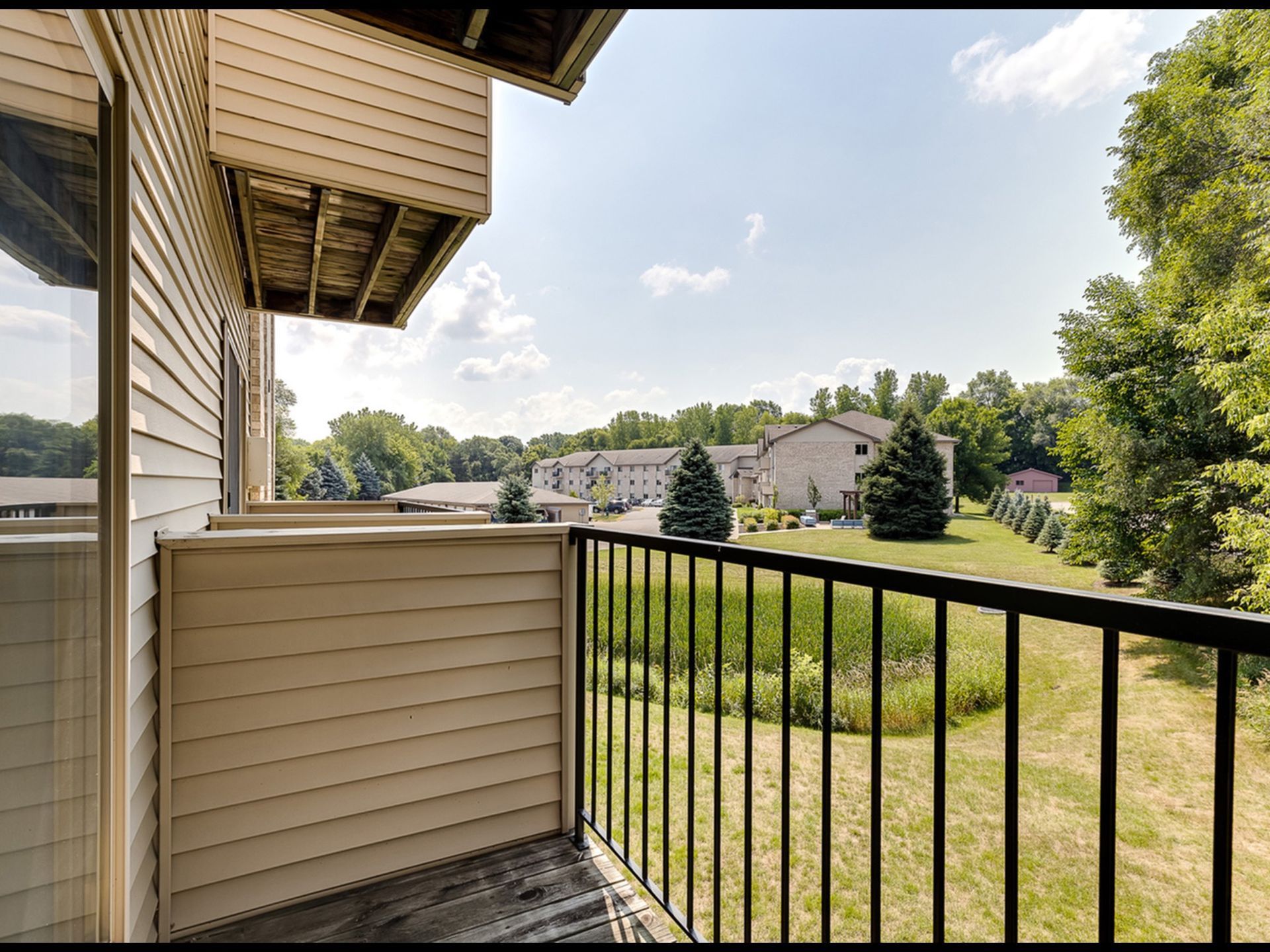 Balcony view from an apartment overlooking the community grounds with buildings and trees.