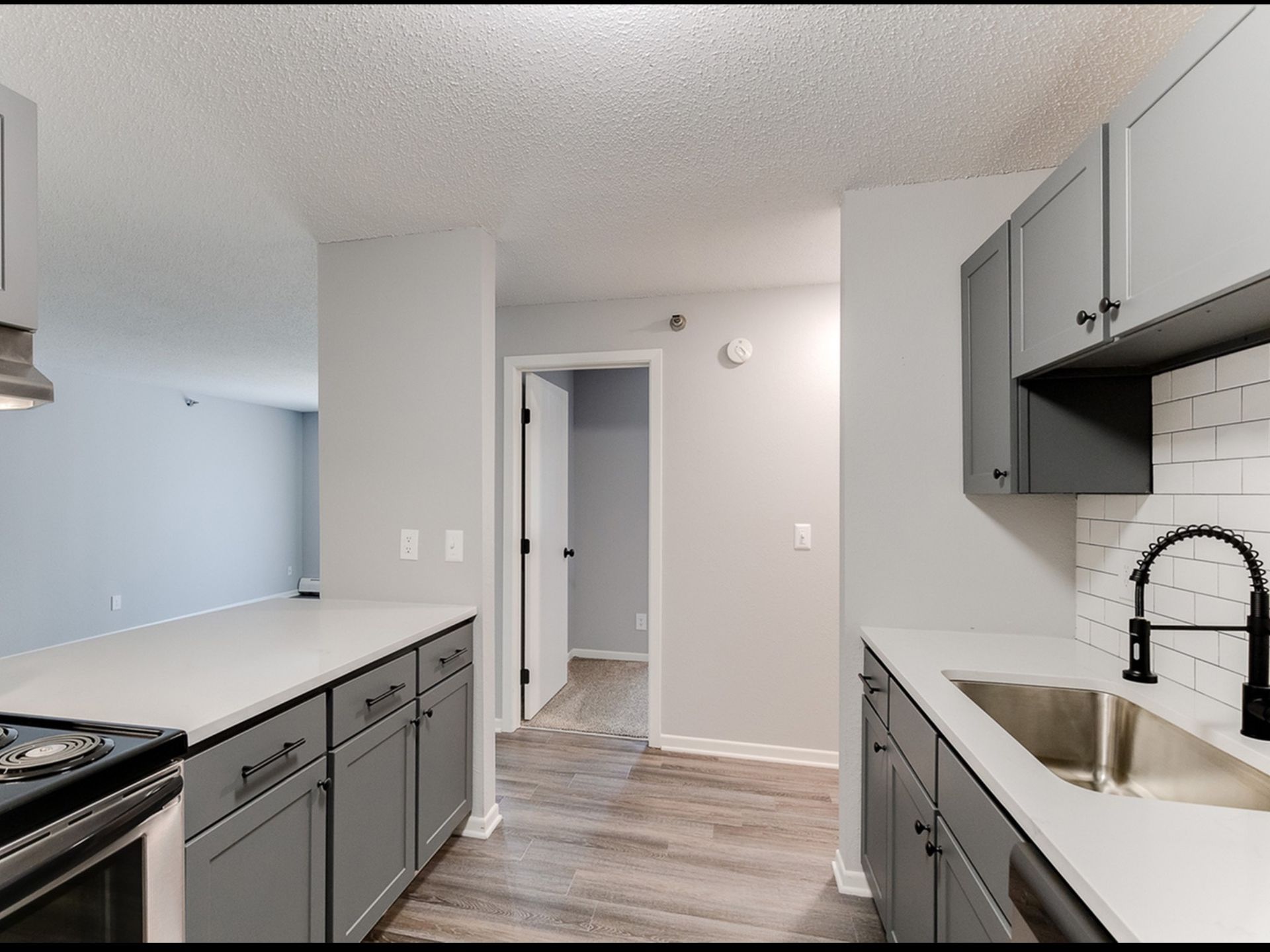 Kitchen in apartment with gray cabinets, white countertops, and stainless steel sink.