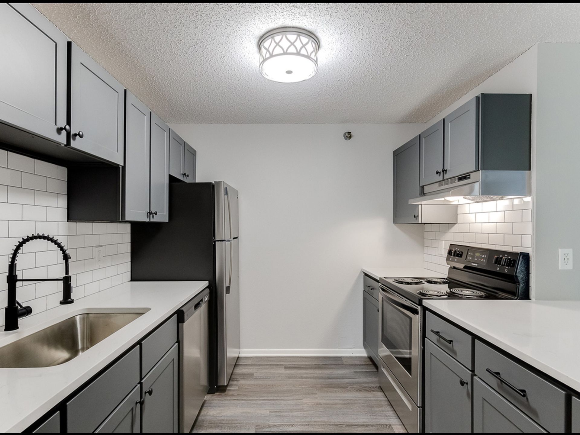 Modern gray kitchen with stainless steel fridge, stove, dishwasher, white counters, and subway tile backsplash.