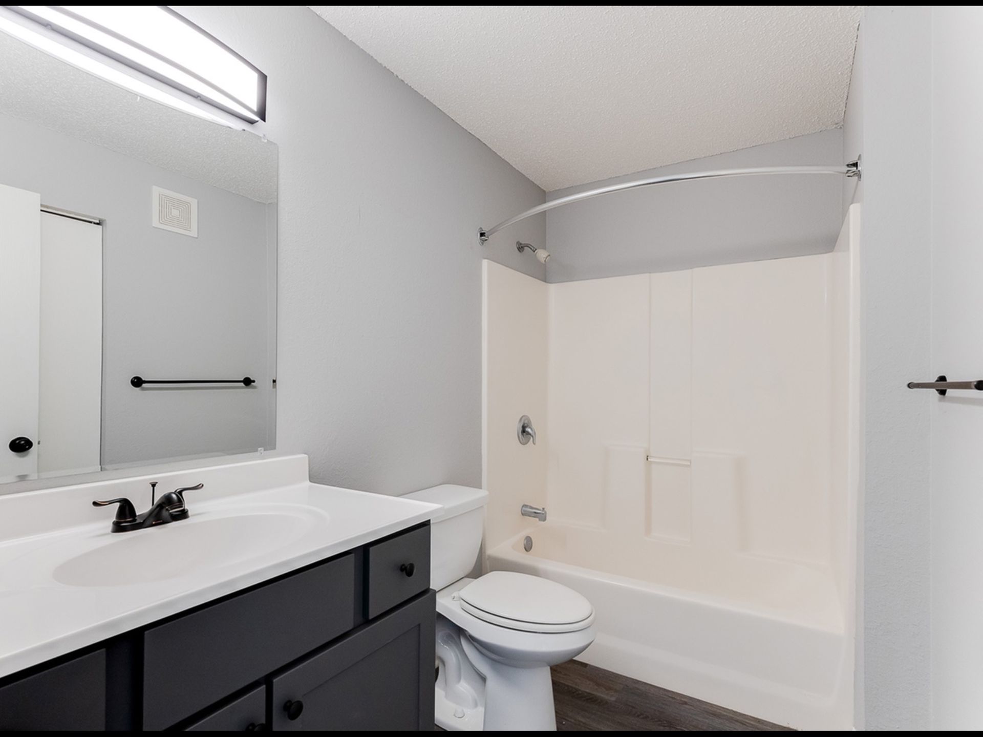Bathroom with white vanity, dark cabinetry, toilet, and tub/shower combo.