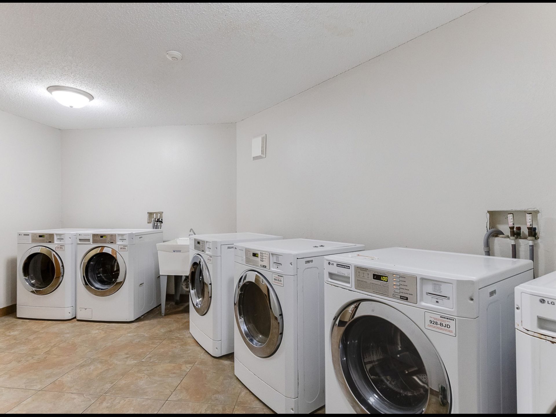 Shared laundry room with multiple front-loading washing machines against white walls.