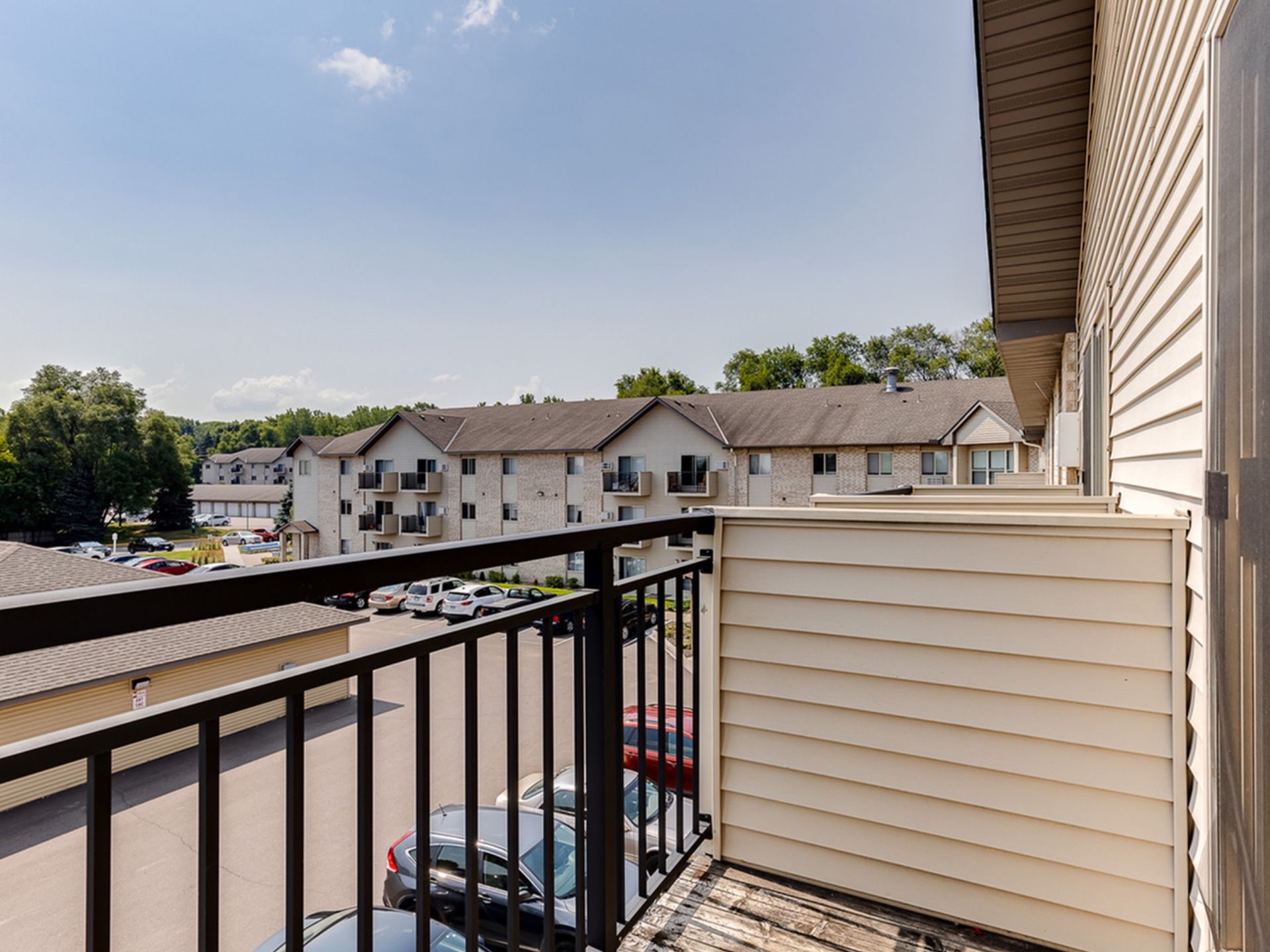 Balcony railing with a view of a multi-building apartment complex and parked cars.