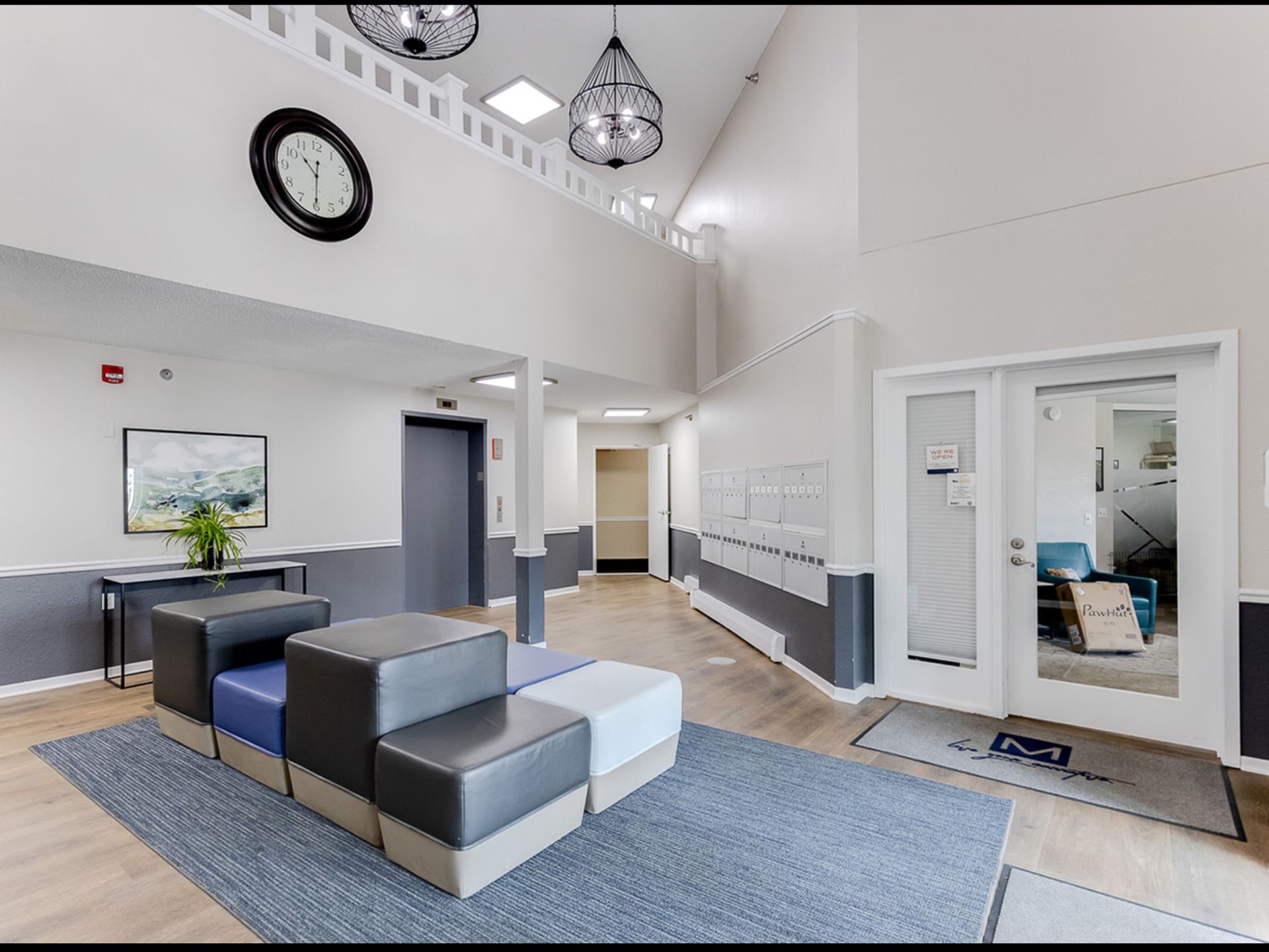 Interior community lobby with modern seating, a wall of mailboxes, and a large clock.