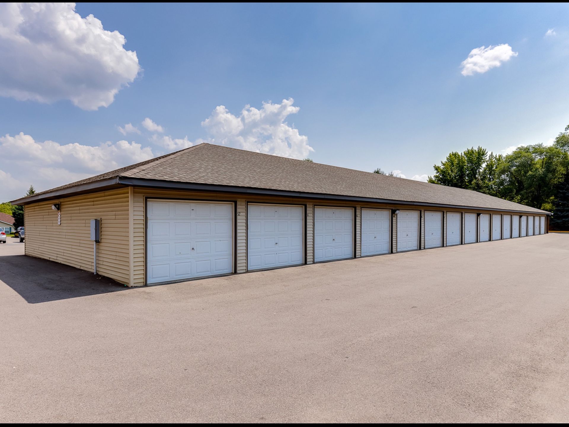 Long row of beige storage units with white doors along a paved lot under a clear blue sky.